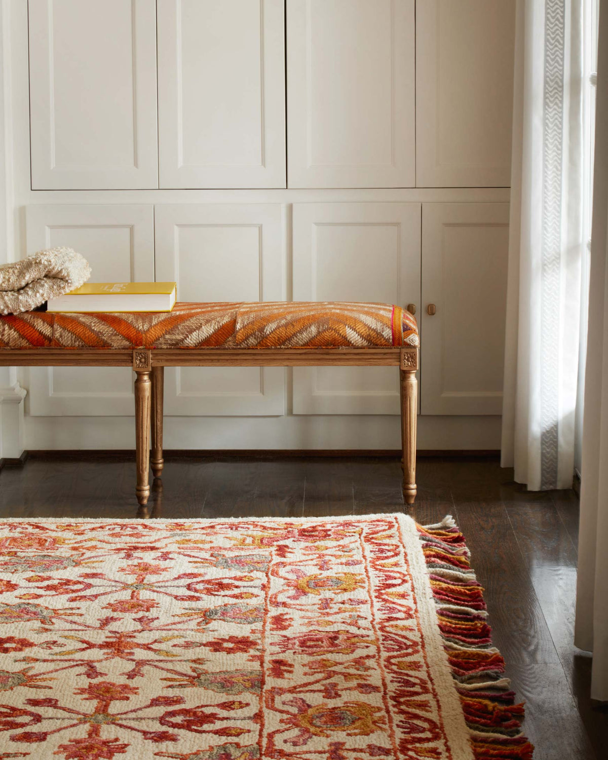 Floral hooked rug in berry tones with fringed edge, shown on dark wood floor