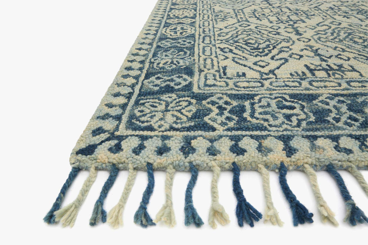 Corner of transitional hooked rug in blue and mist with detailed pattern and fringe