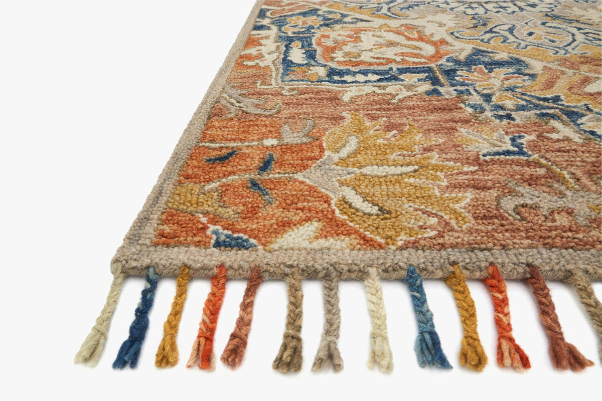 Corner view of rust and blue hooked rug with multicolor fringe tassels