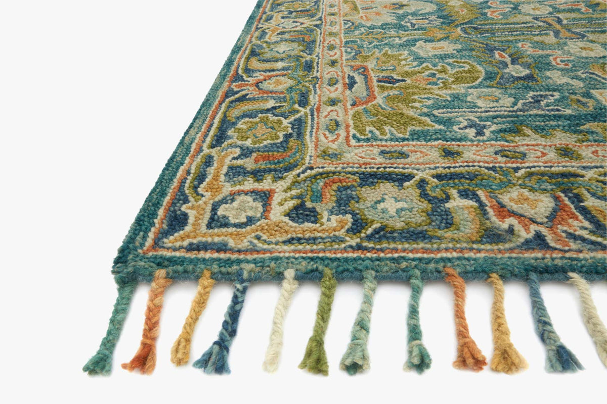 Corner view of hooked area rug in blue tones with detailed pattern and fringe.