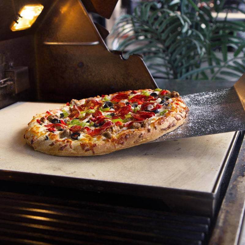 Pizza baking on beige ceramic stone set in stainless steel tray