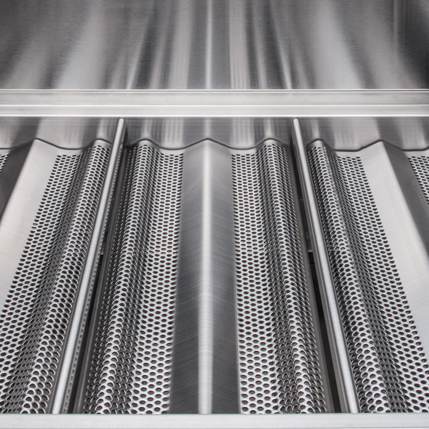 Close-up of perforated stainless burner surfaces inside the grill firebox.