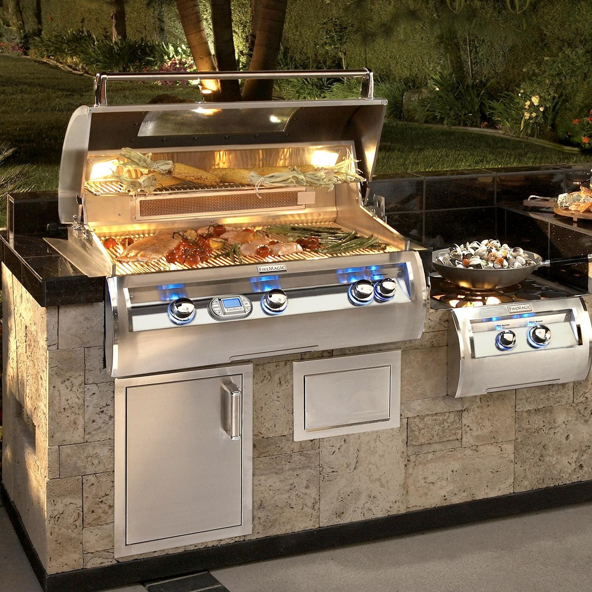 Built-in stainless gas grill with open lid, illuminated burners, and front controls
