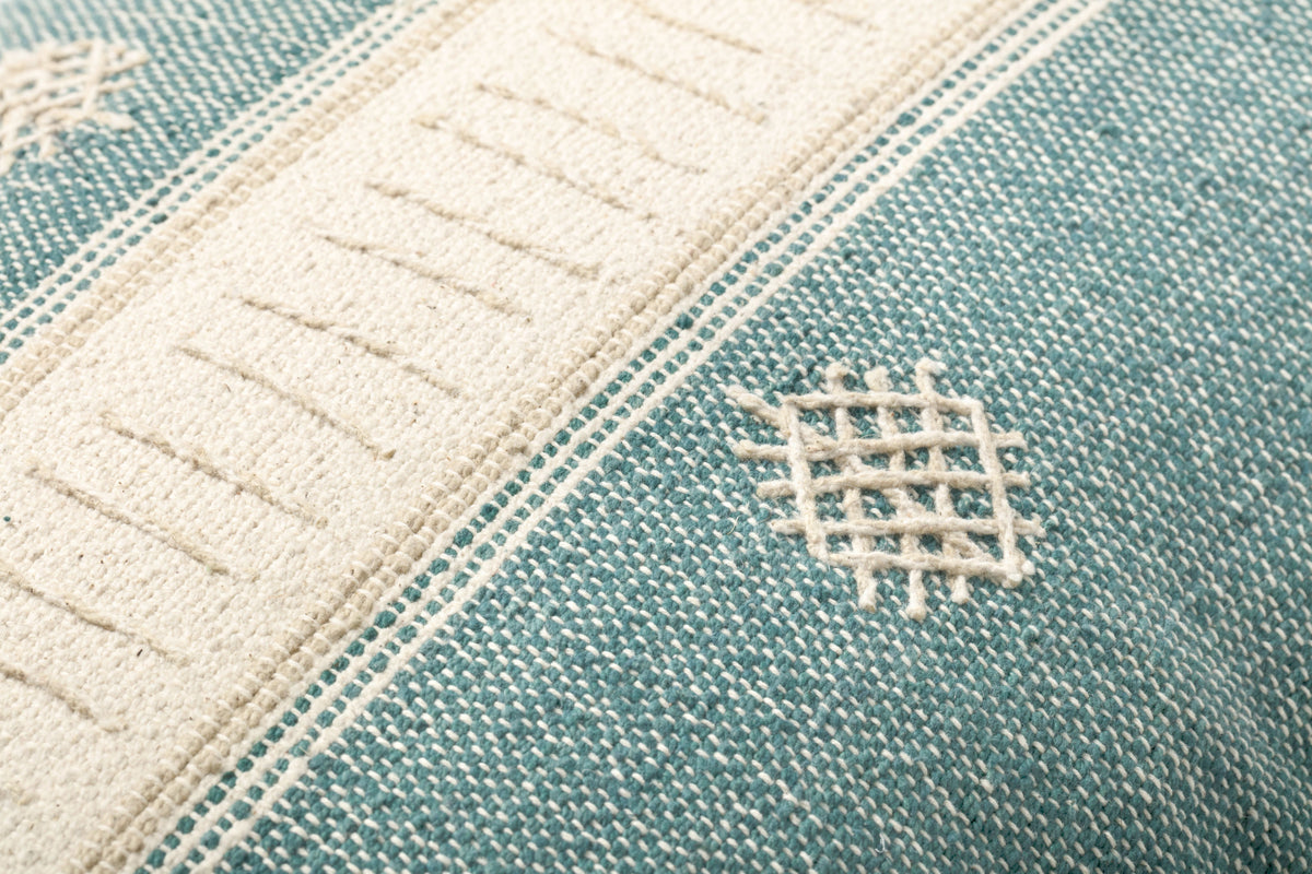 Teal fabric pillow corner with lattice embroidery and stitched cream border