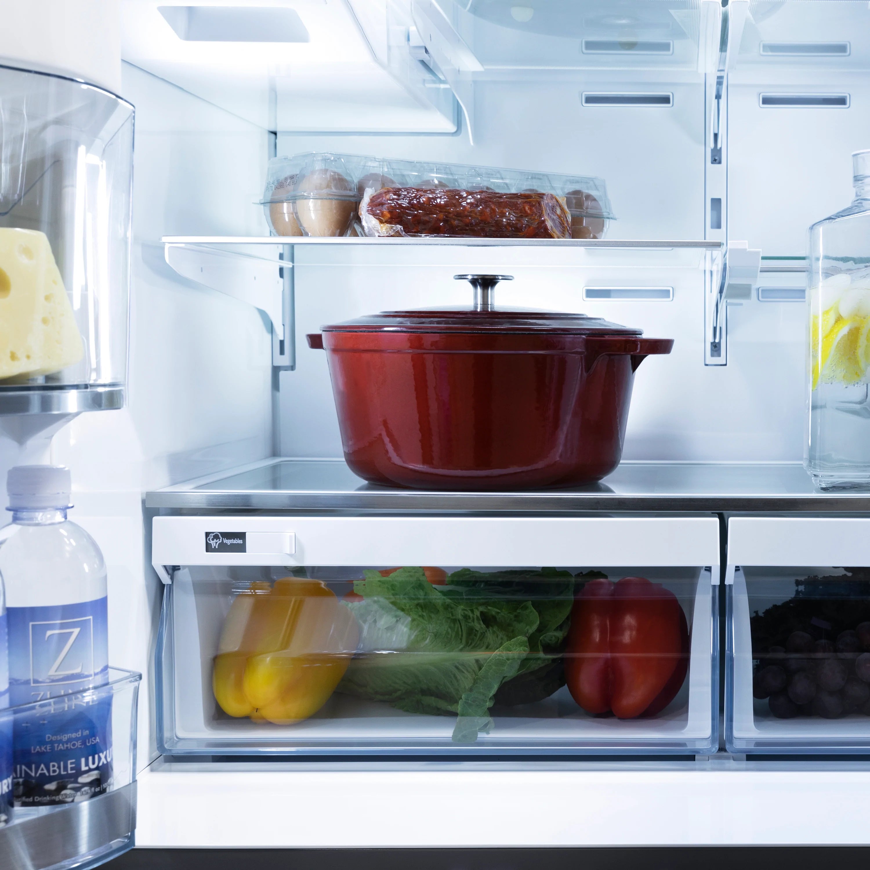 Refrigerator interior with red pot, covered dish, and produce on middle shelves