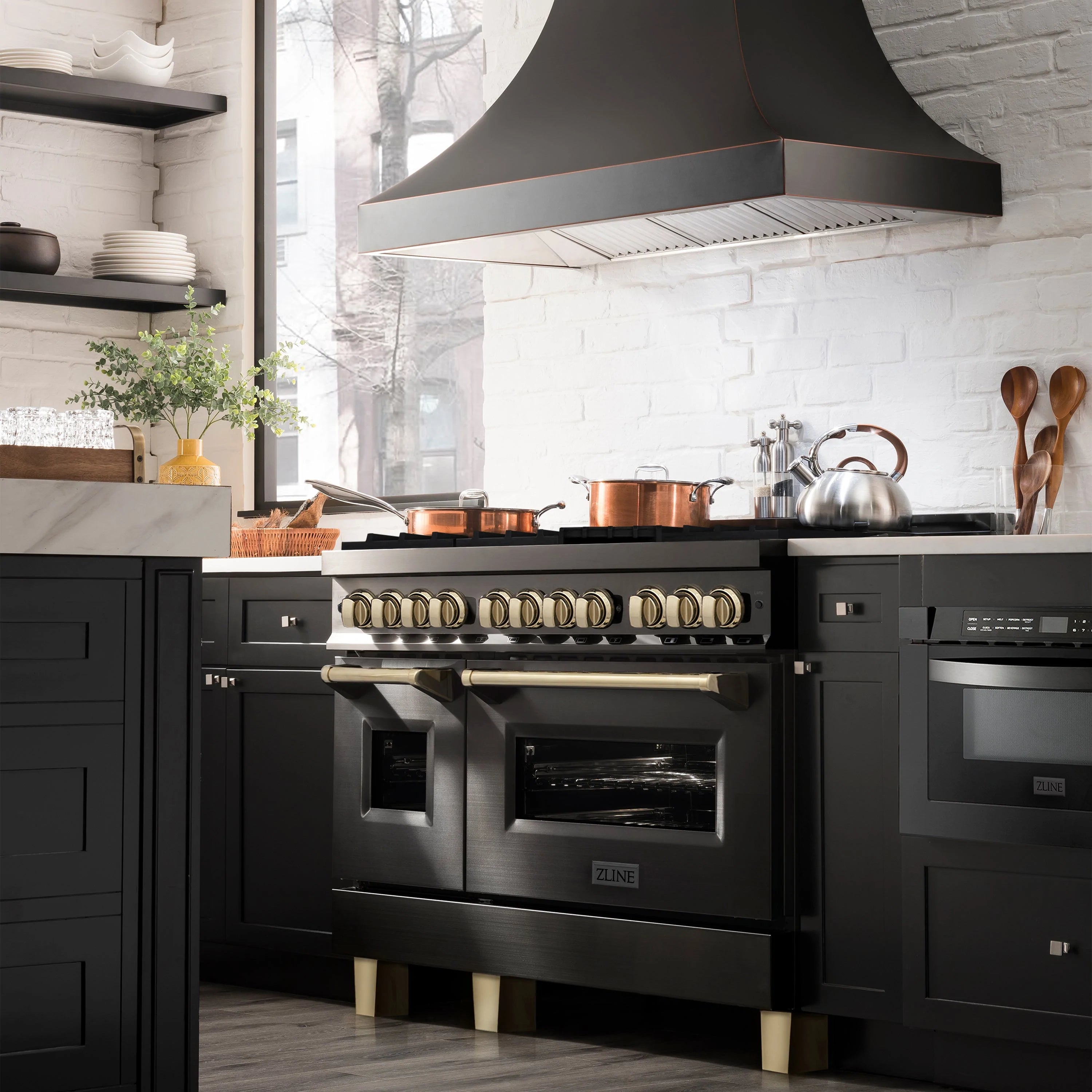 Black stainless dual fuel range with gold-trimmed controls and wall-mounted range hood