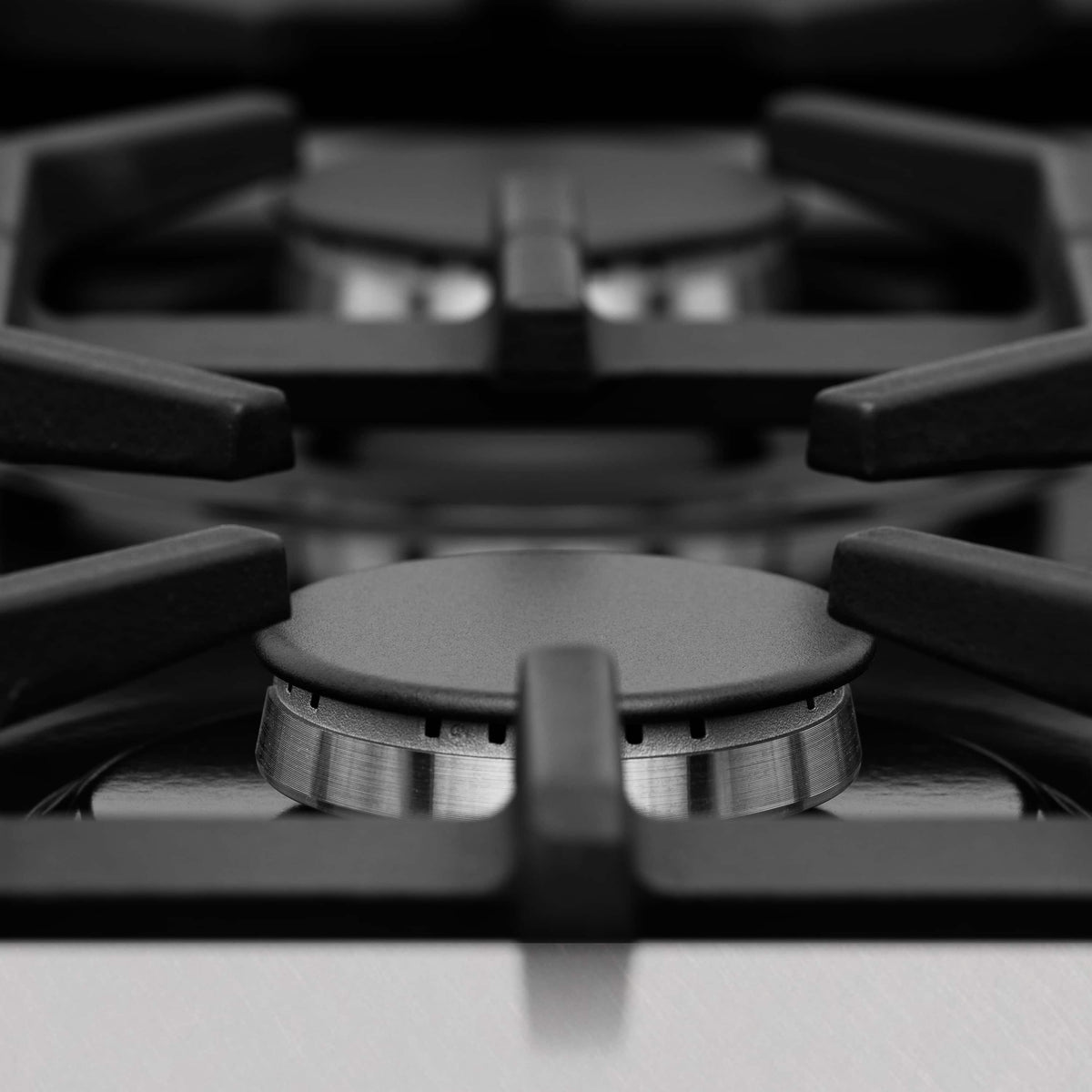 Gas cooktop burner head with round metal grate and black control knobs