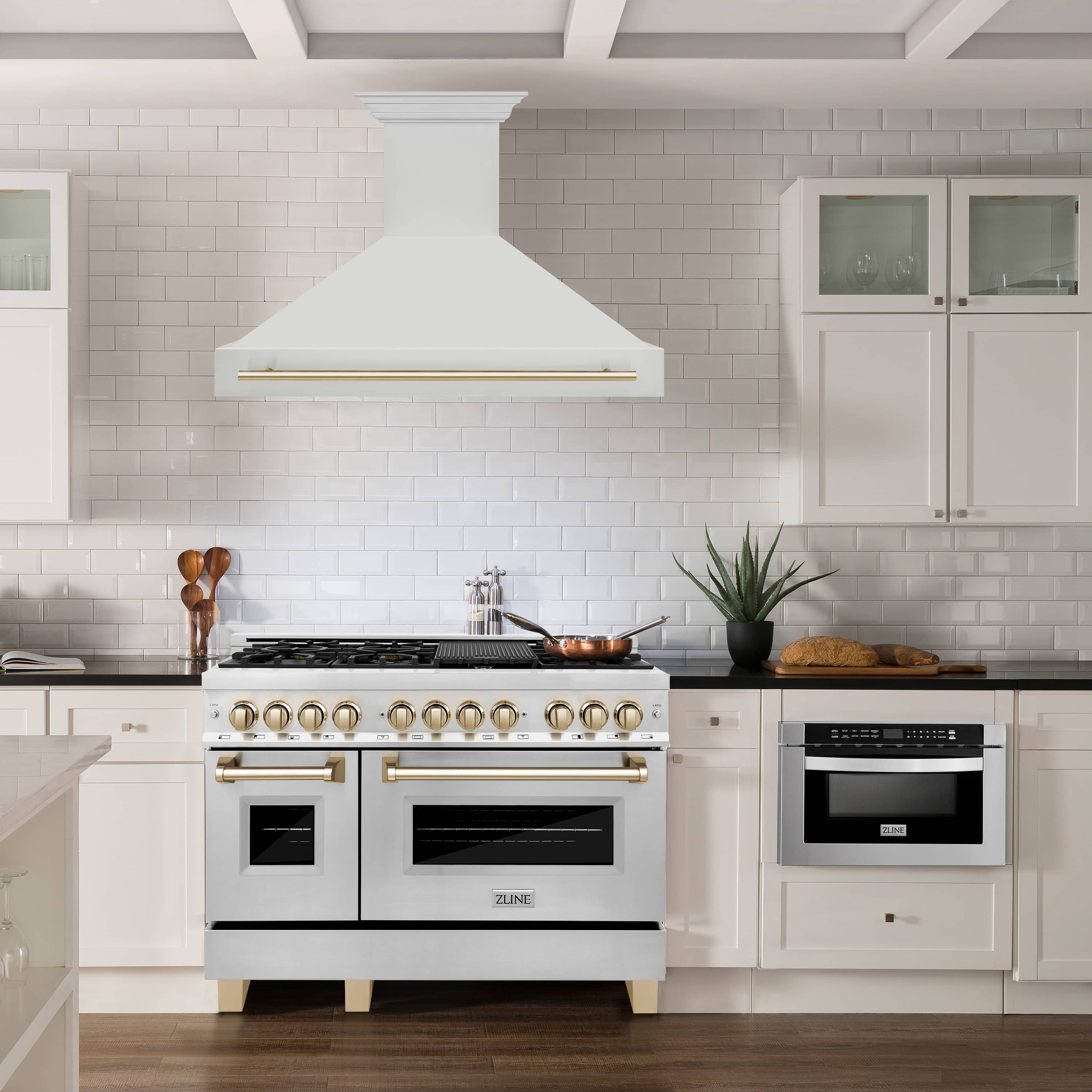 White wall-mount range hood with gold handle bar above a cooktop