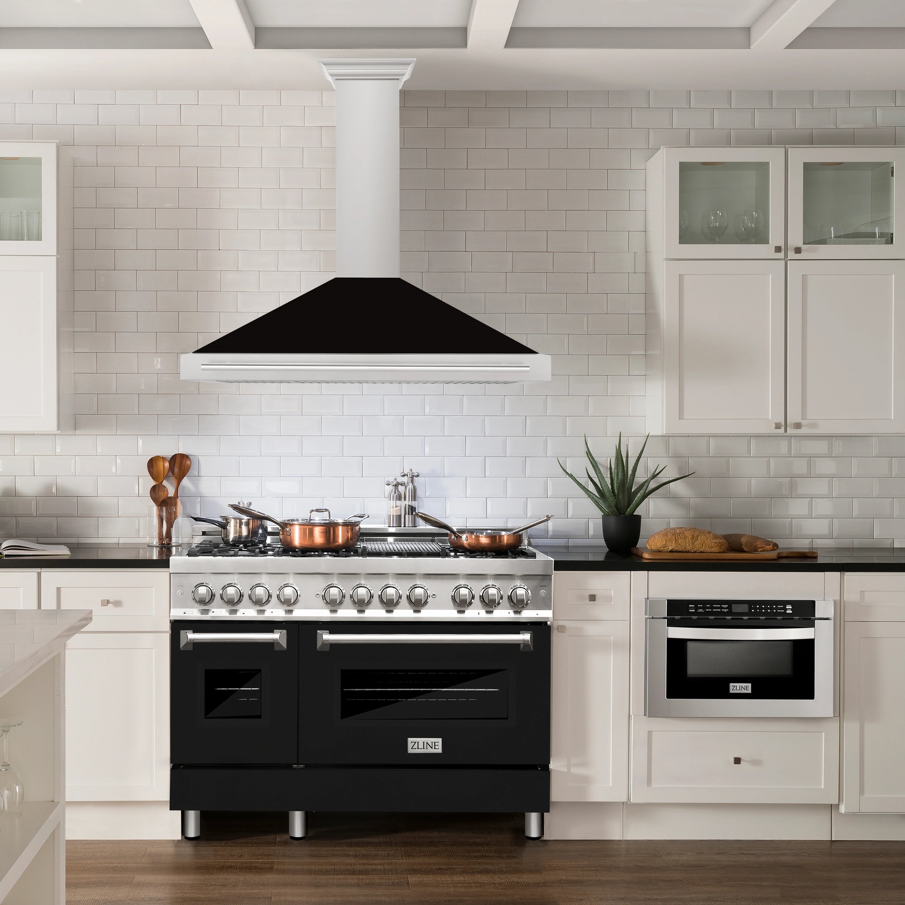 Wall-mounted range hood with black canopy over stainless cooktop and oven