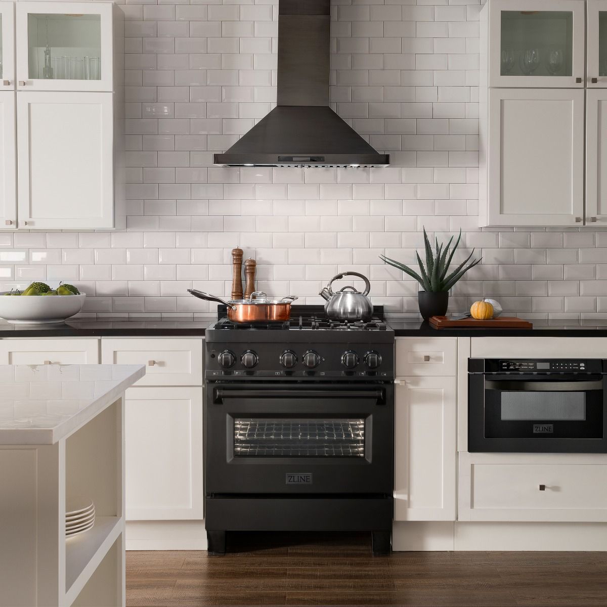 Black stainless range with brass burners and wall hood in kitchen scene.