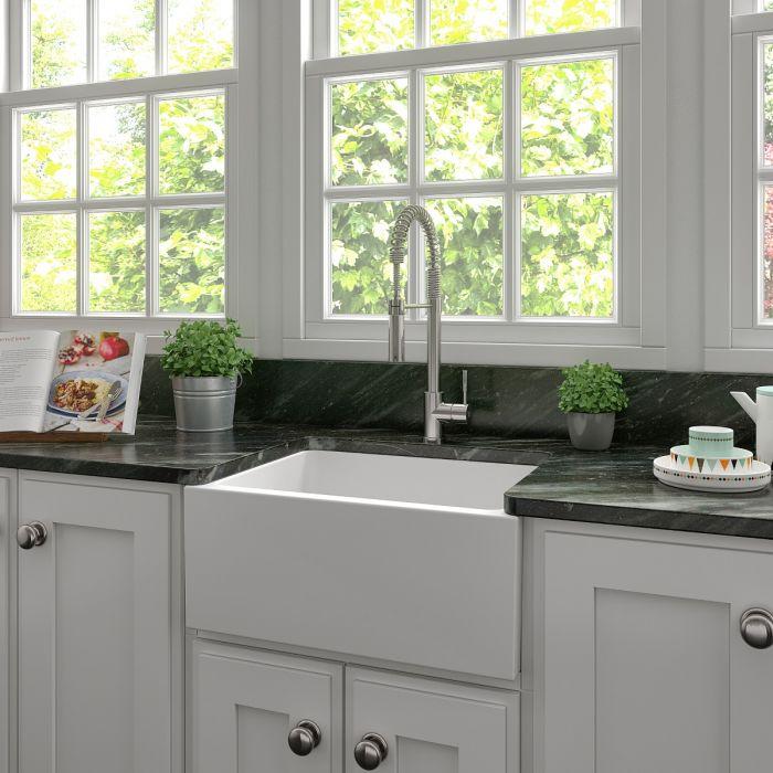 White matte apron-front farmhouse kitchen sink with single bowl, faucet, and countertop
