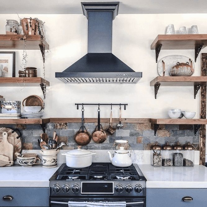 Black wall range hood with chimney installed above a cooktop in a kitchen.