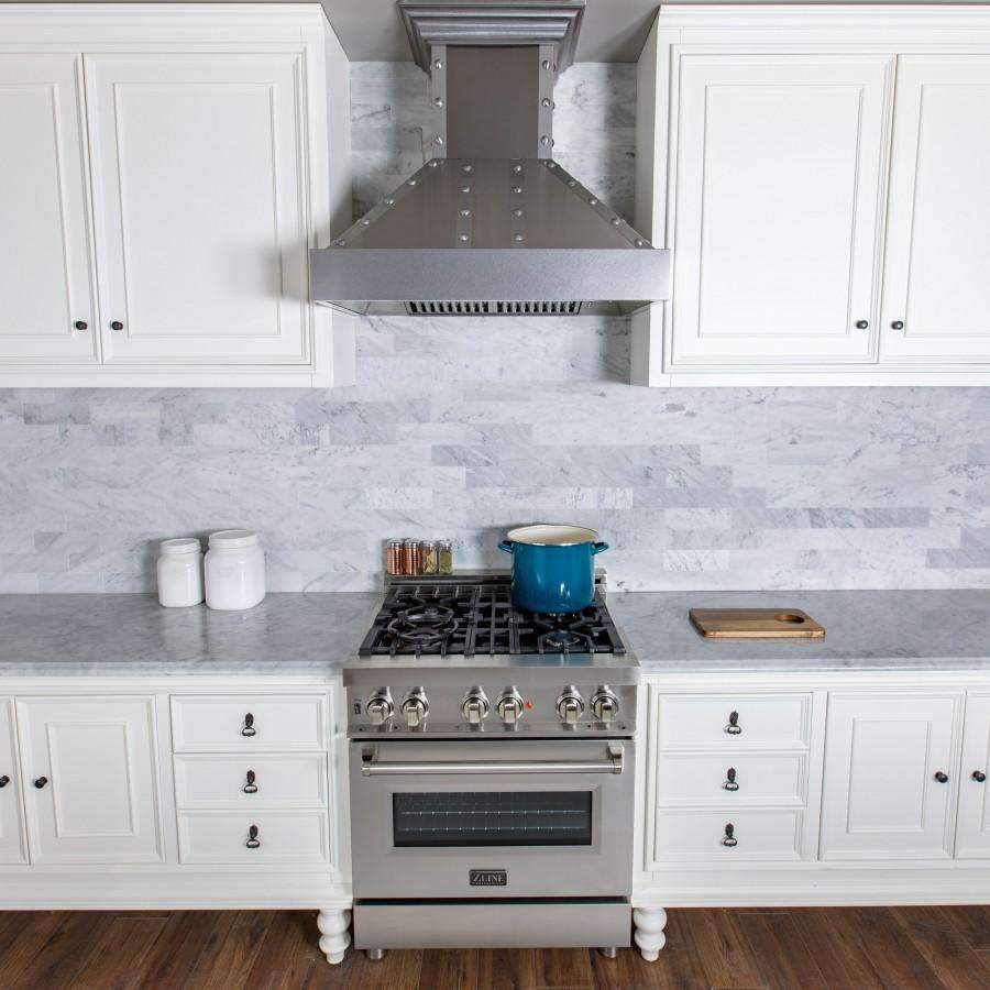 Stainless dual fuel range with black grates, brass burner caps, and lit oven window.