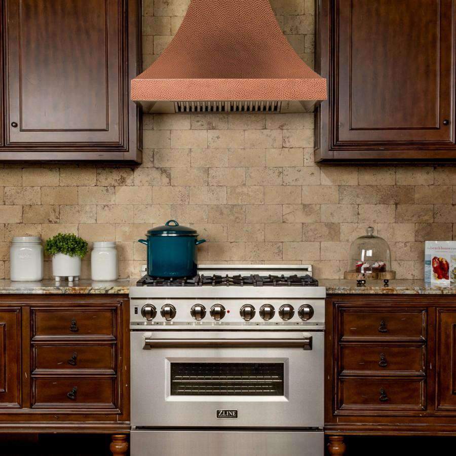 Wall range hood with hand-hammered copper chimney over stainless gas cooktop