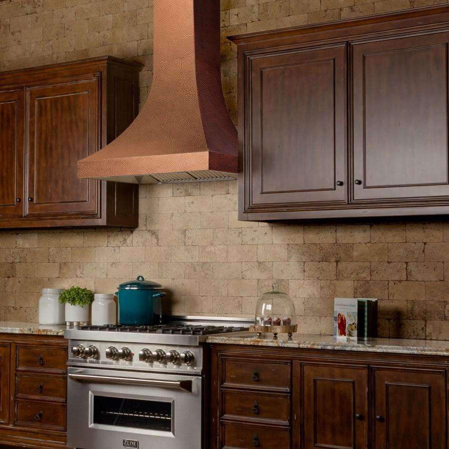 Hand-hammered copper wall range hood with stainless vent canopy above gas cooktop