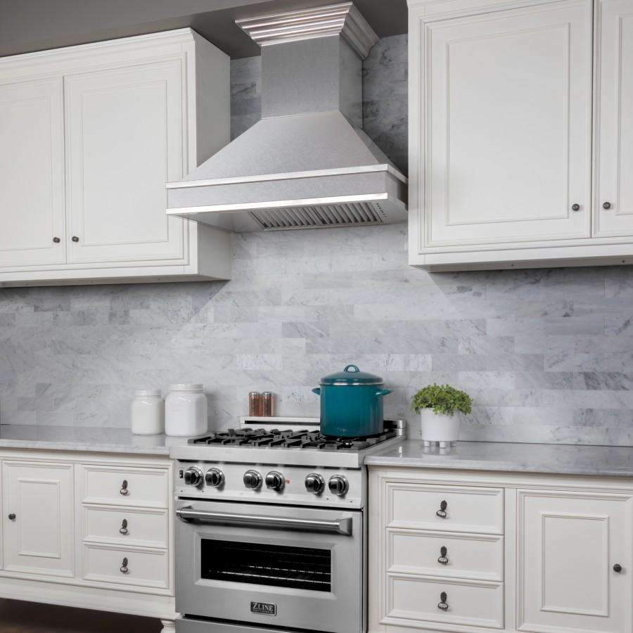 Satin stainless steel wall mount range hood above a gas cooktop