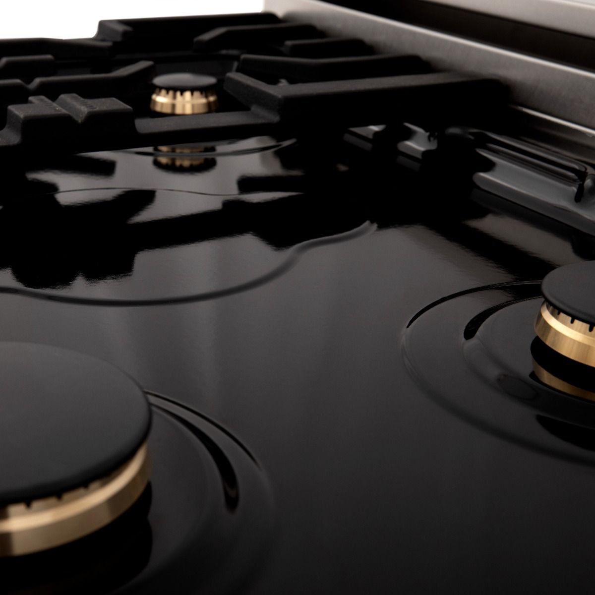 Black gas cooktop with brass burner caps and black grates, angled view of multiple burners