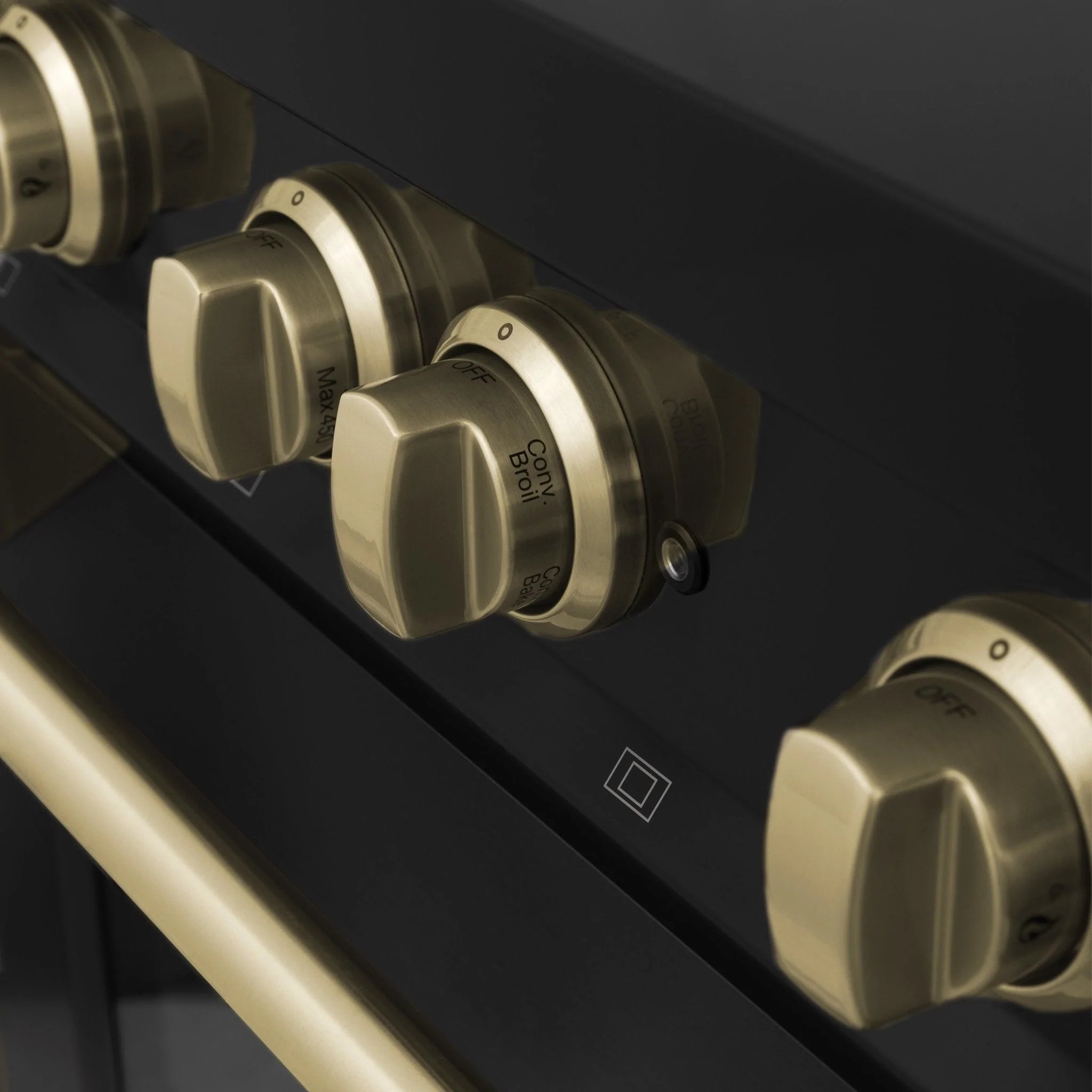 Close-up of champagne bronze control knobs on a black stainless range panel