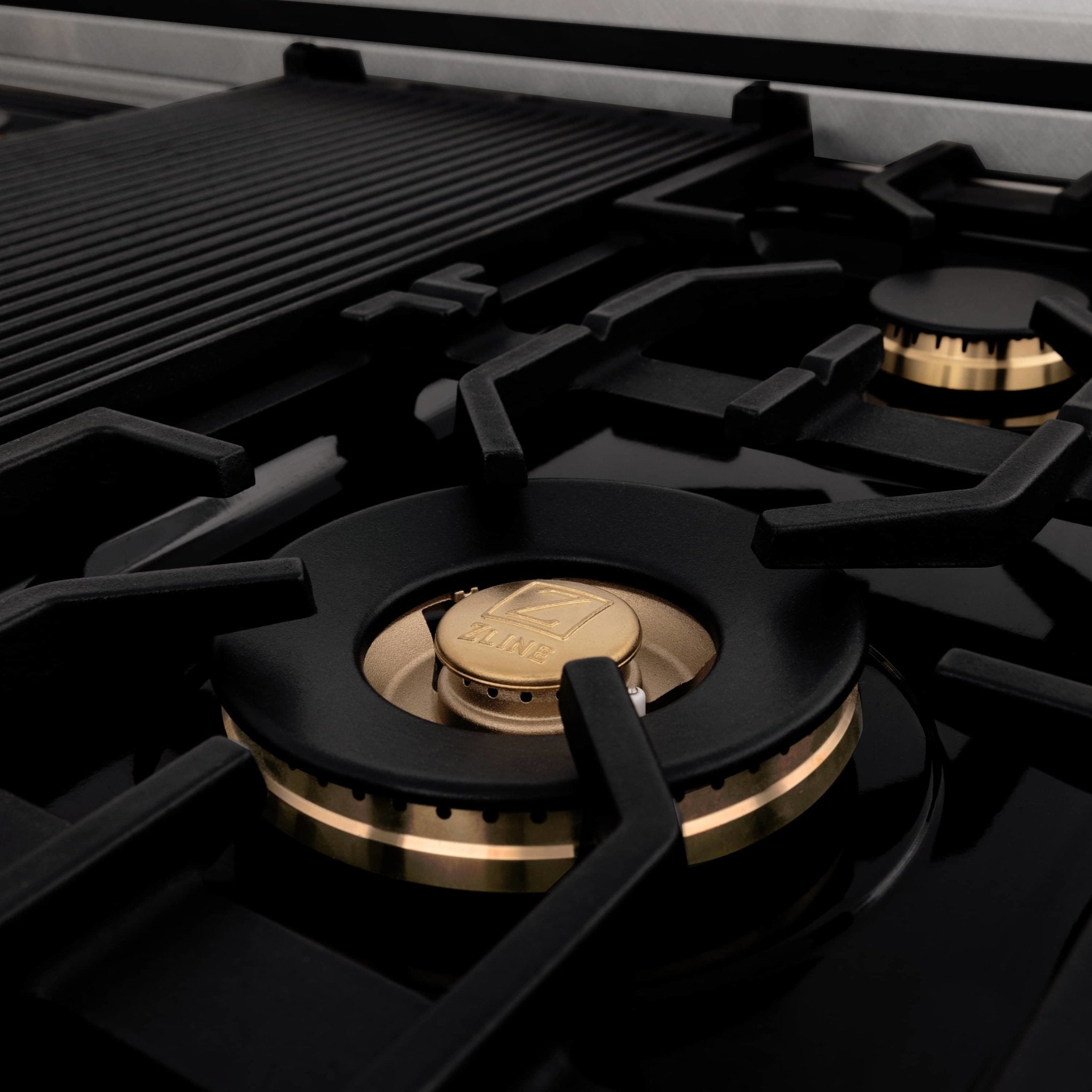 Gas cooktop burner with black grate and gold ring accents on dual-fuel range