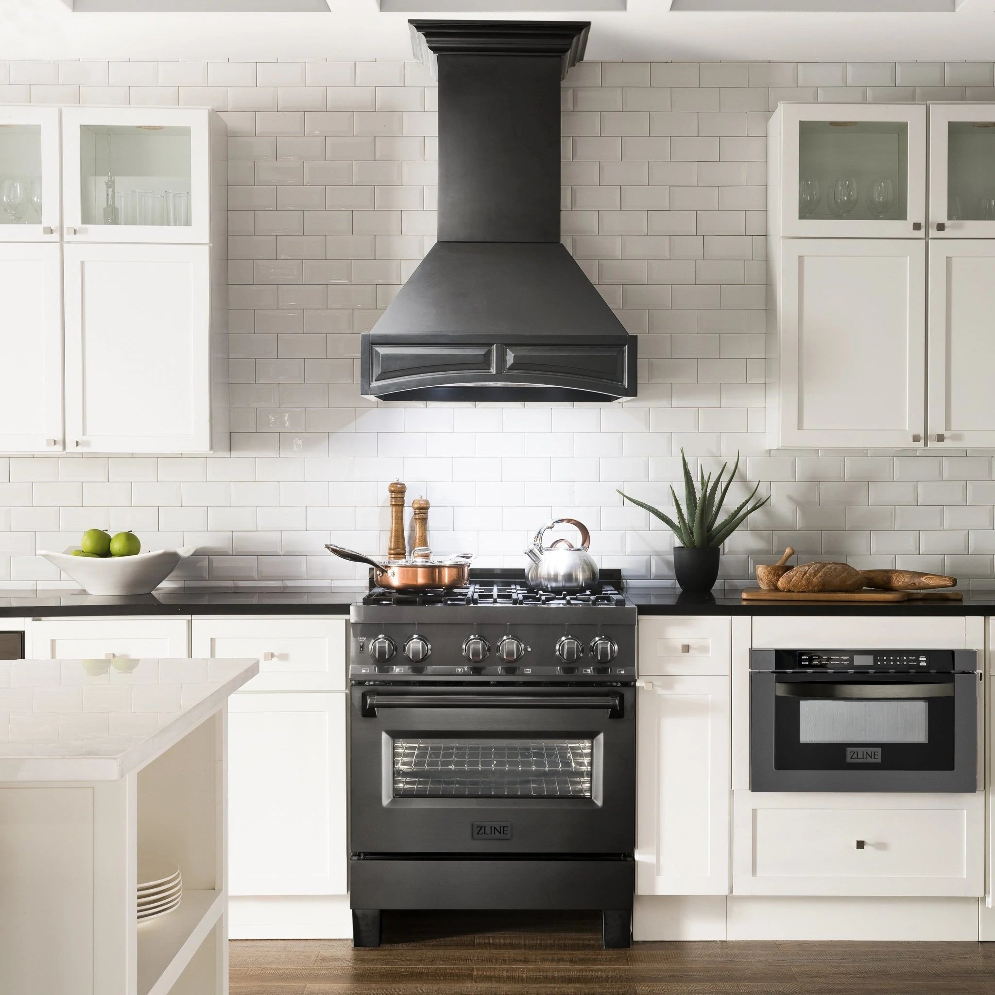 Black chimney wall range hood over a stainless range with cabinets and backsplash tiles