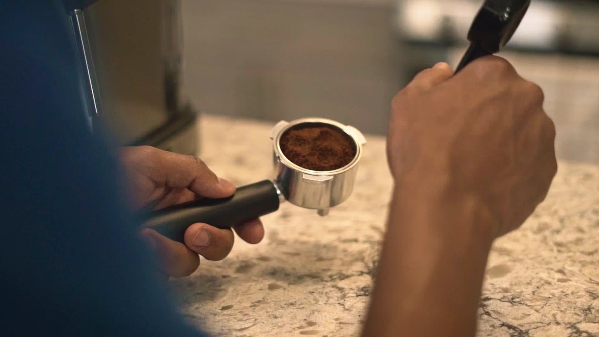 Hands holding portafilter with brewed coffee, ready to remove from espresso machine