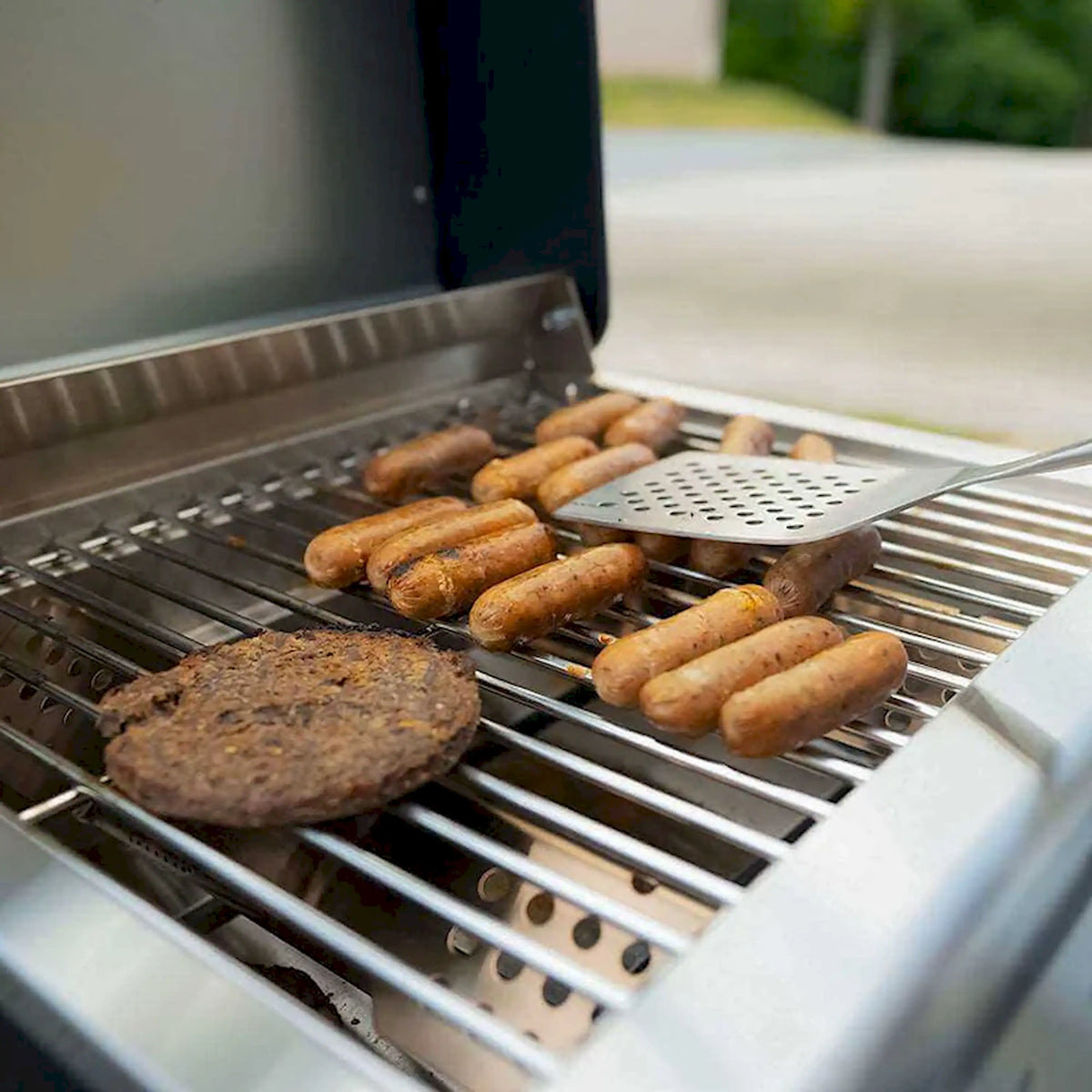 Tabletop propane gas grill grates with sausages and a burger patty cooking