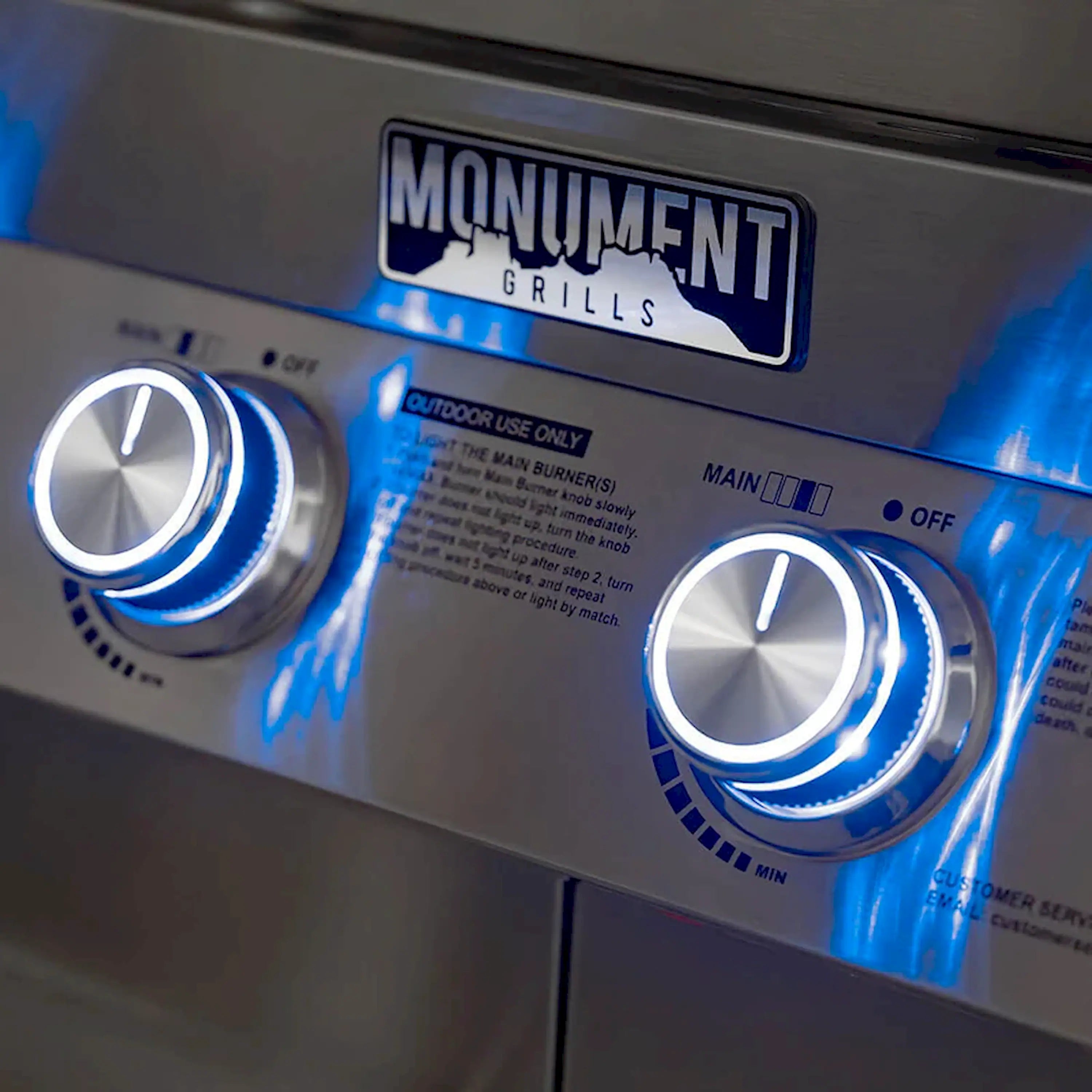 Stainless steel control panel with Monument Grills logo and blue-lit temperature knobs