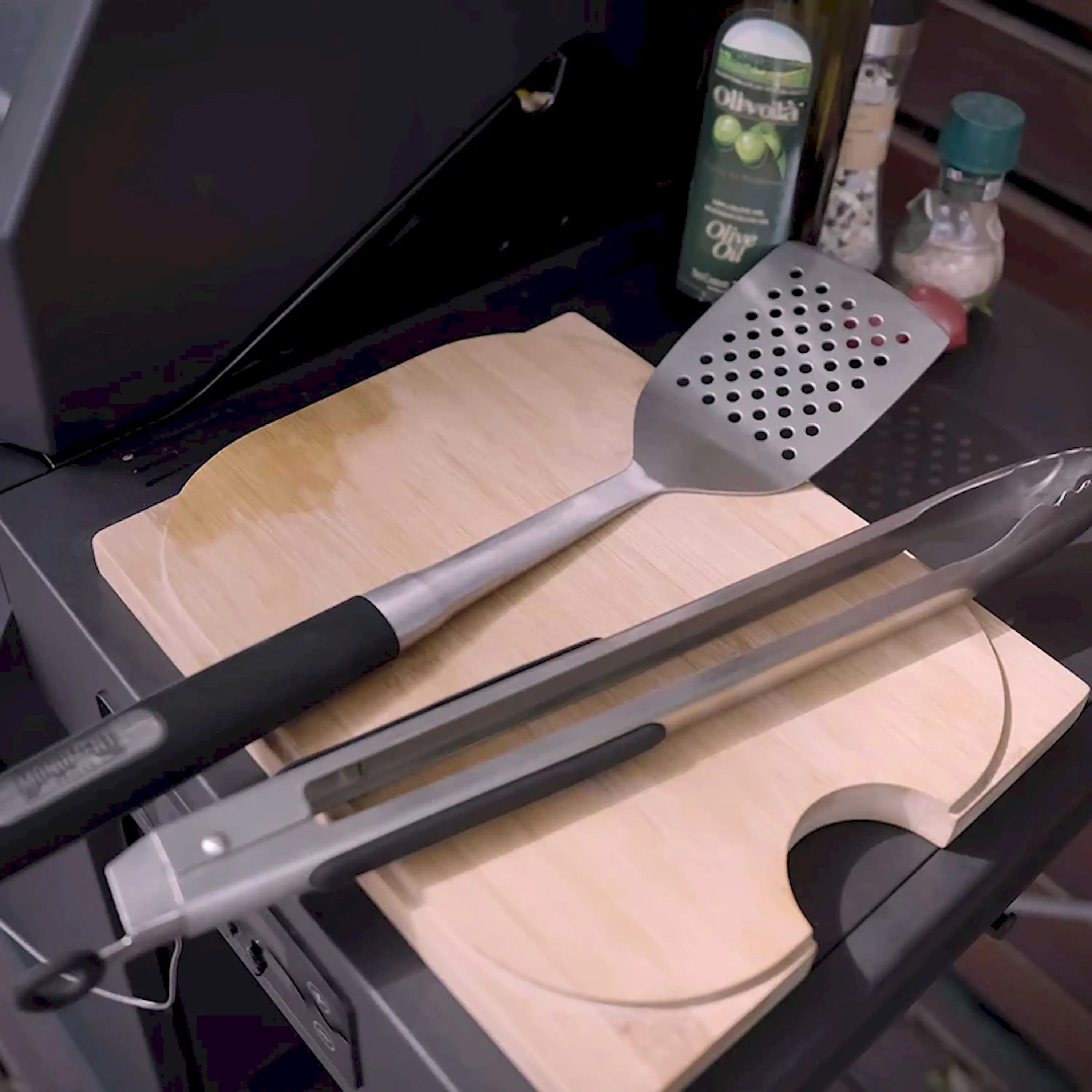 Perforated spatula and slotted tong with black handles on wooden cutting board