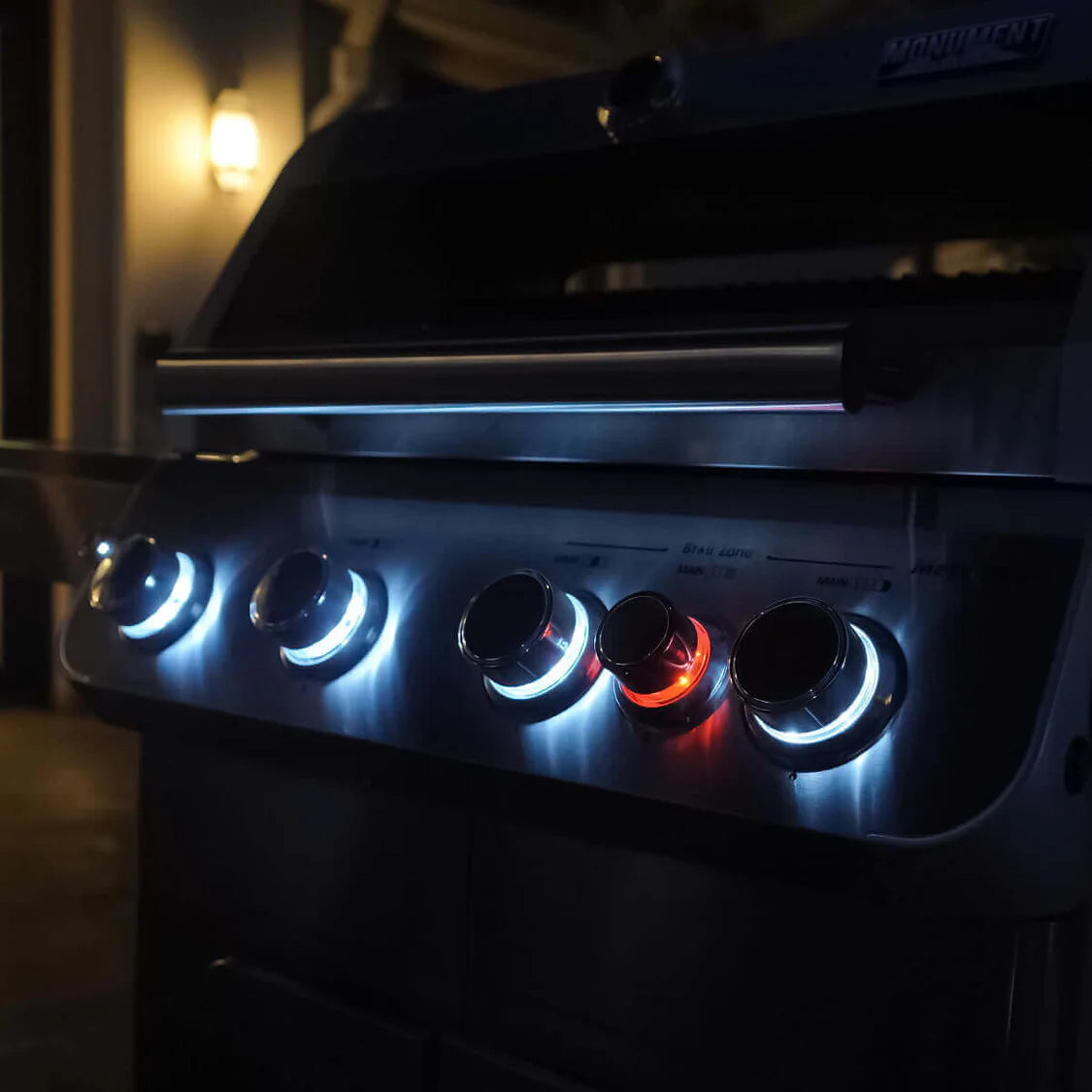 Front view of stainless steel propane gas grill with four burners glowing blue and orange