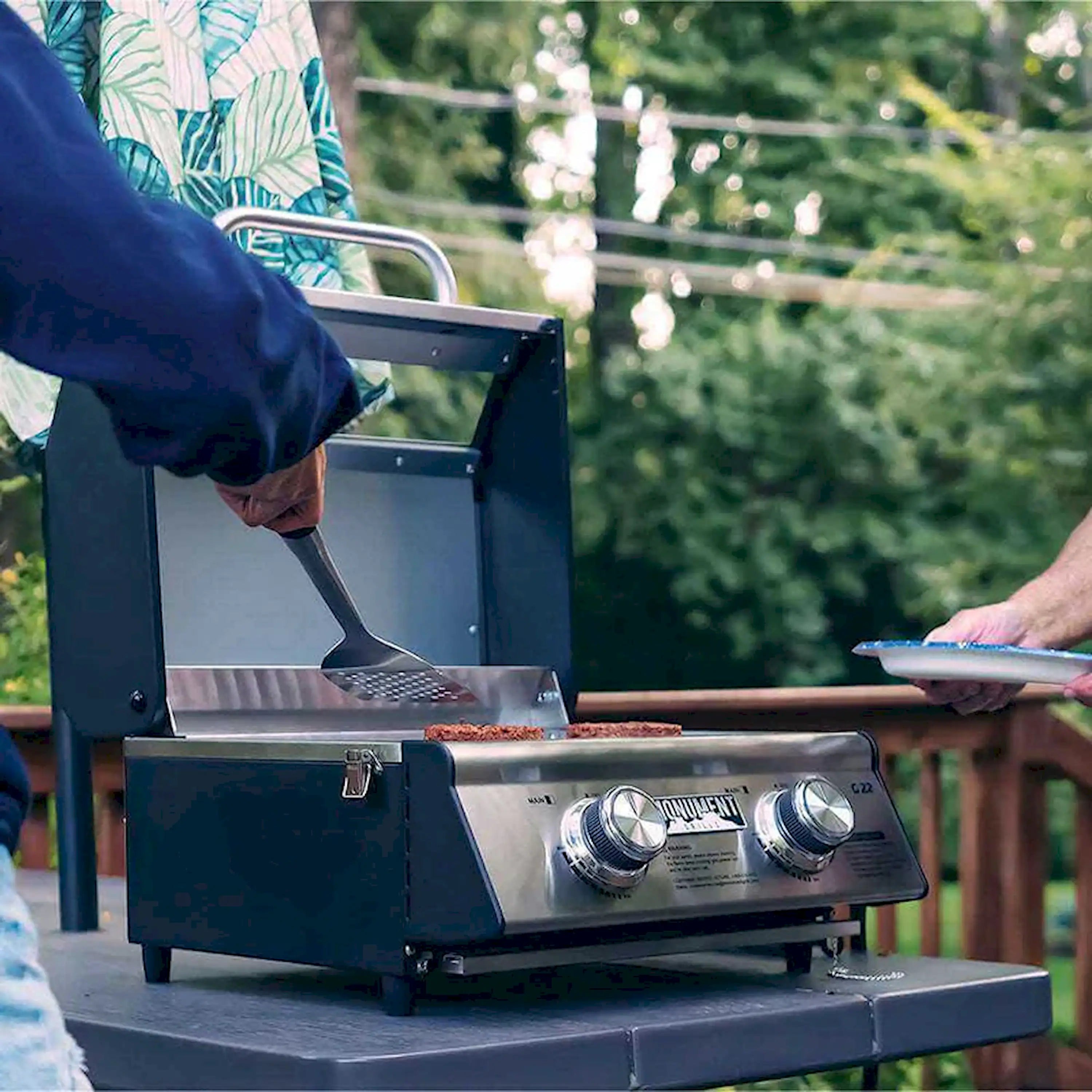 Tabletop propane grill with lid open and meat being placed on the grates