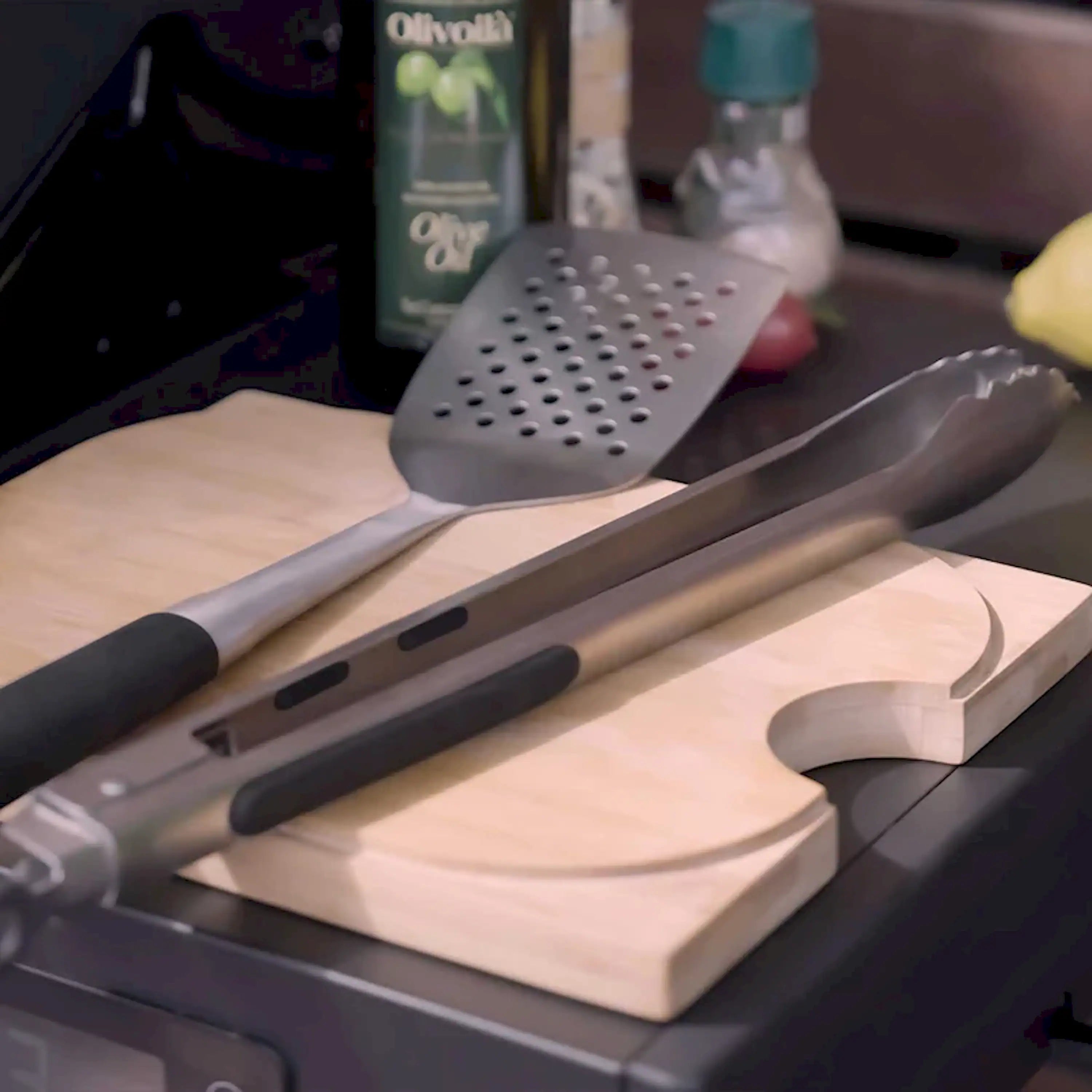 Perforated spatula and slotted tong with black handles on wooden cutting board