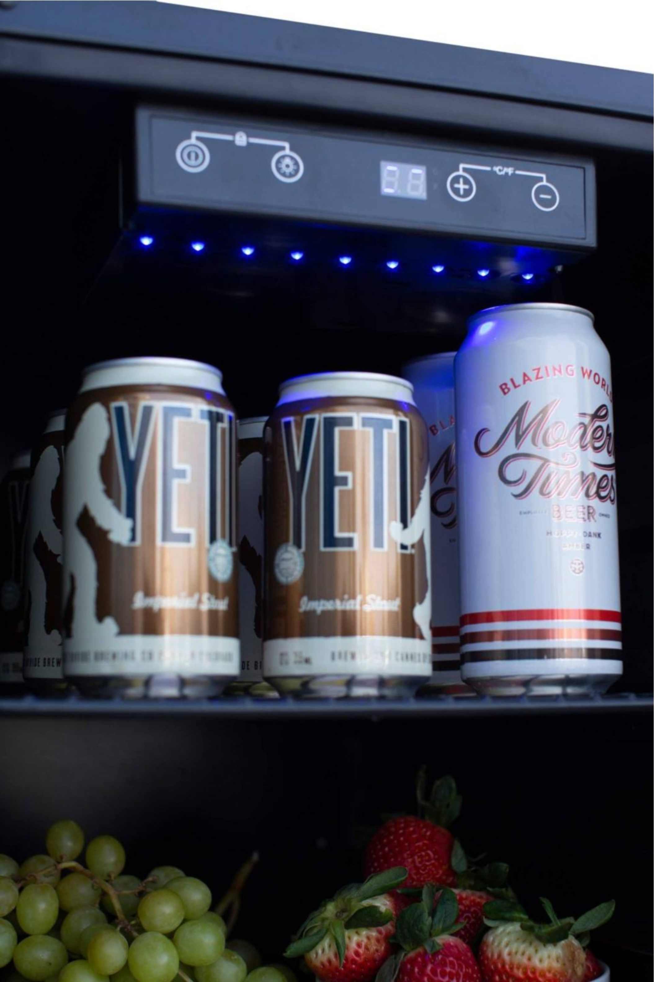 Outdoor refrigerator interior with lit control panel and rows of beverage cans