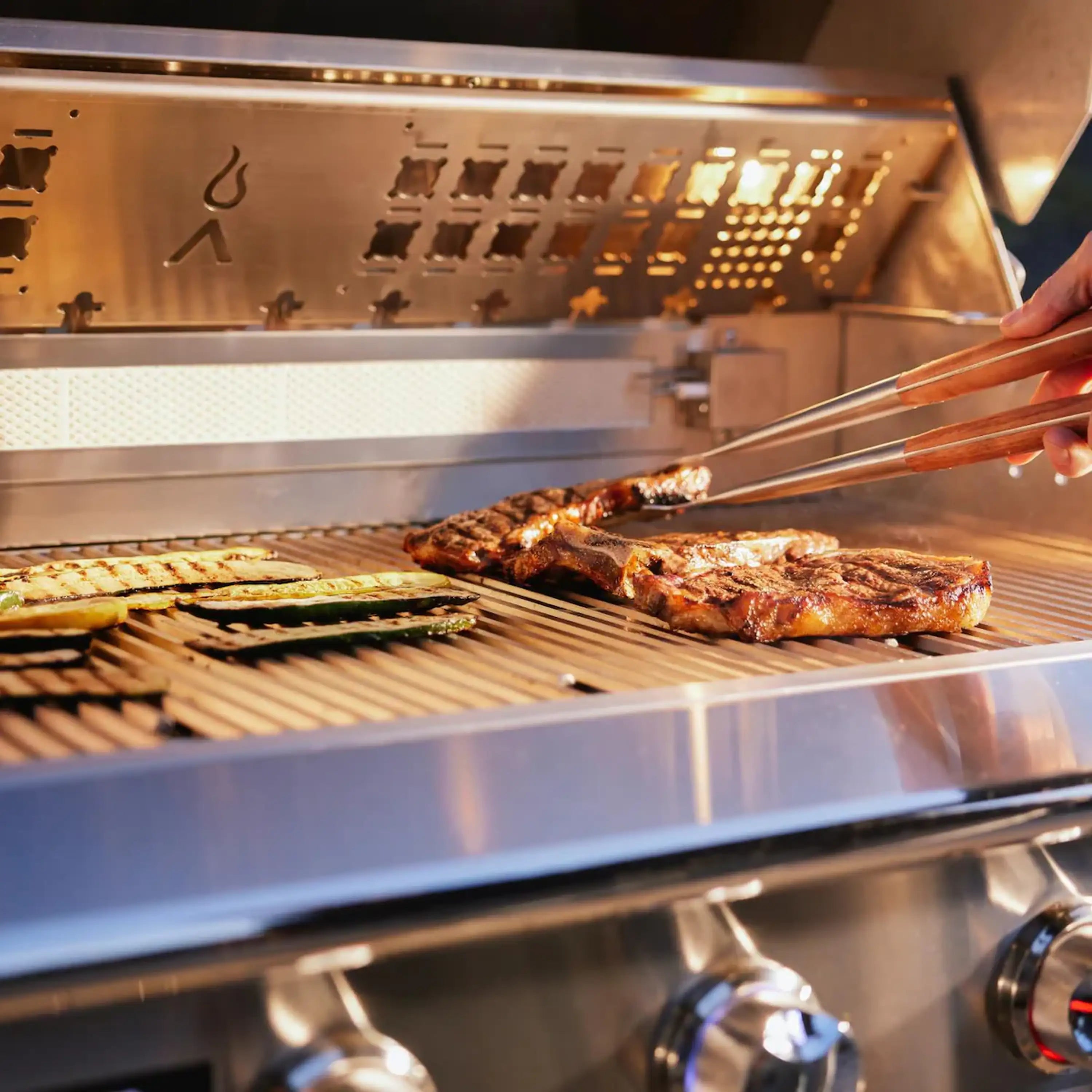 Food grilling on stainless steel grates inside a built-in natural gas grill with lid open