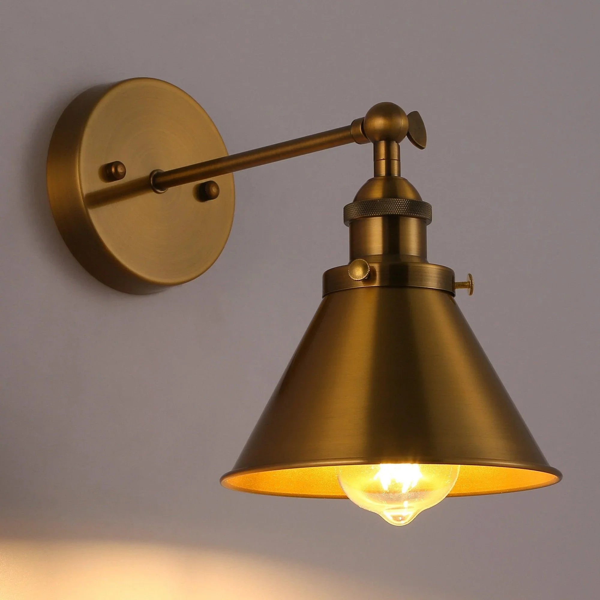 Golden brass wall sconce with bell shade and glowing filament bulb under the shade
