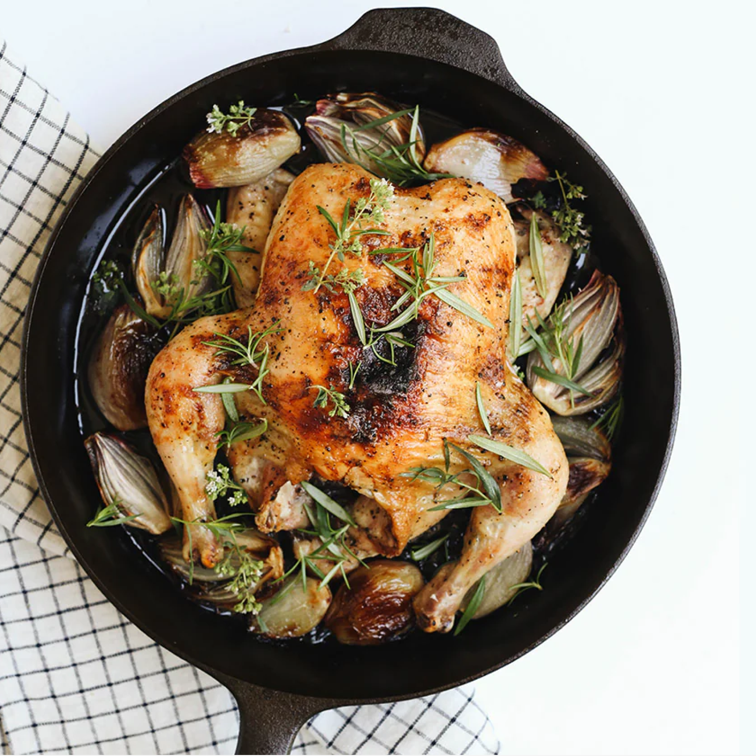 Dark cast-iron skillet with cooked chicken and herbs