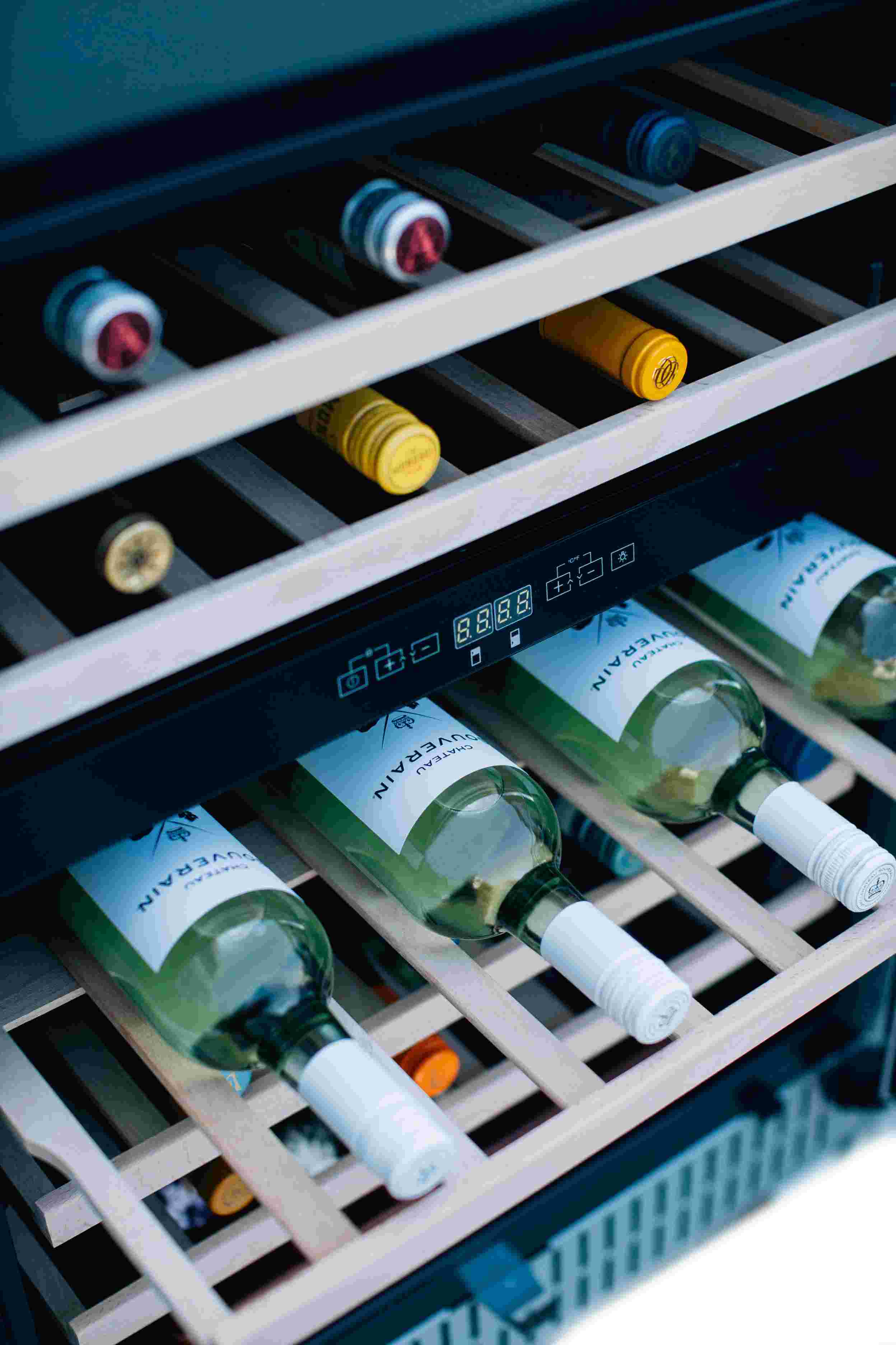 Dual-zone wine cooler interior with sliding racks and bottles on white wooden shelves