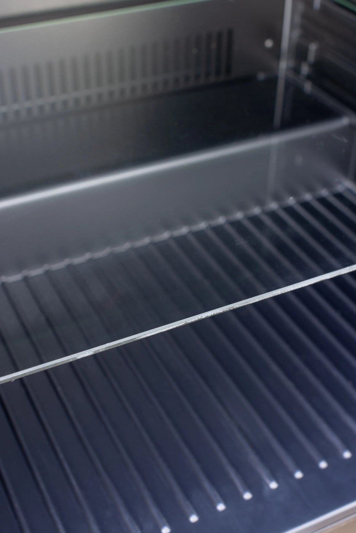 Outdoor fridge interior with dark bottom grill and wire shelving rails