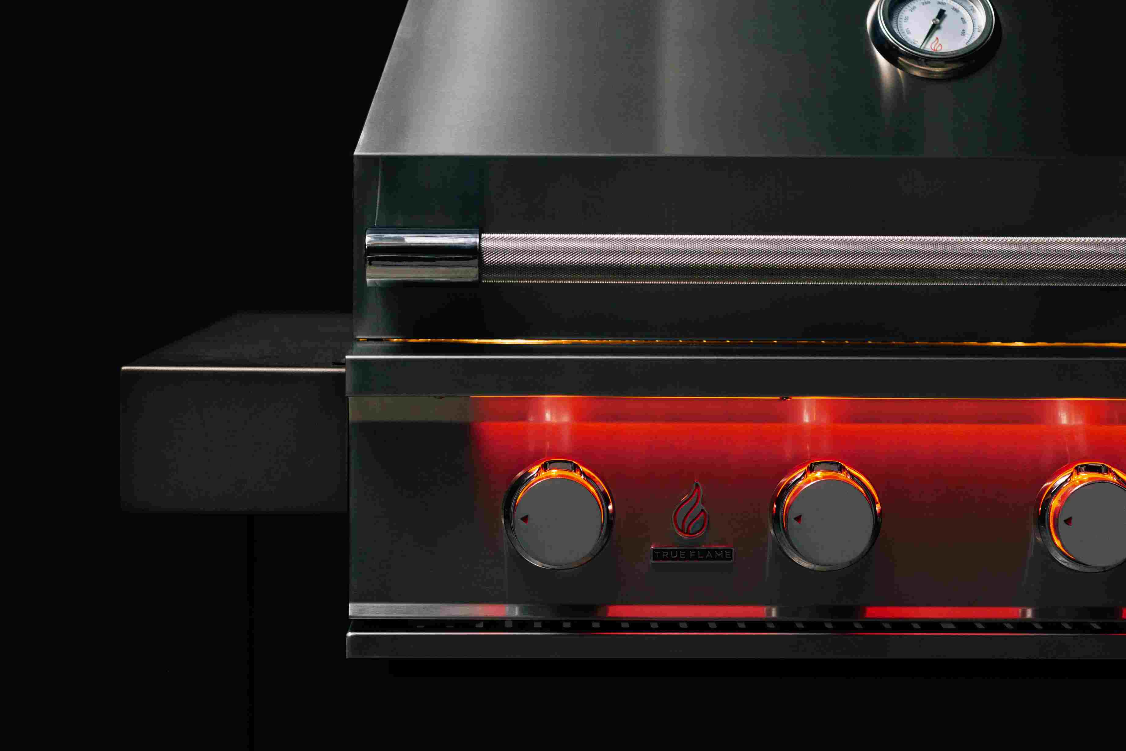 Stainless steel gas grill front controls with lit burners underneath