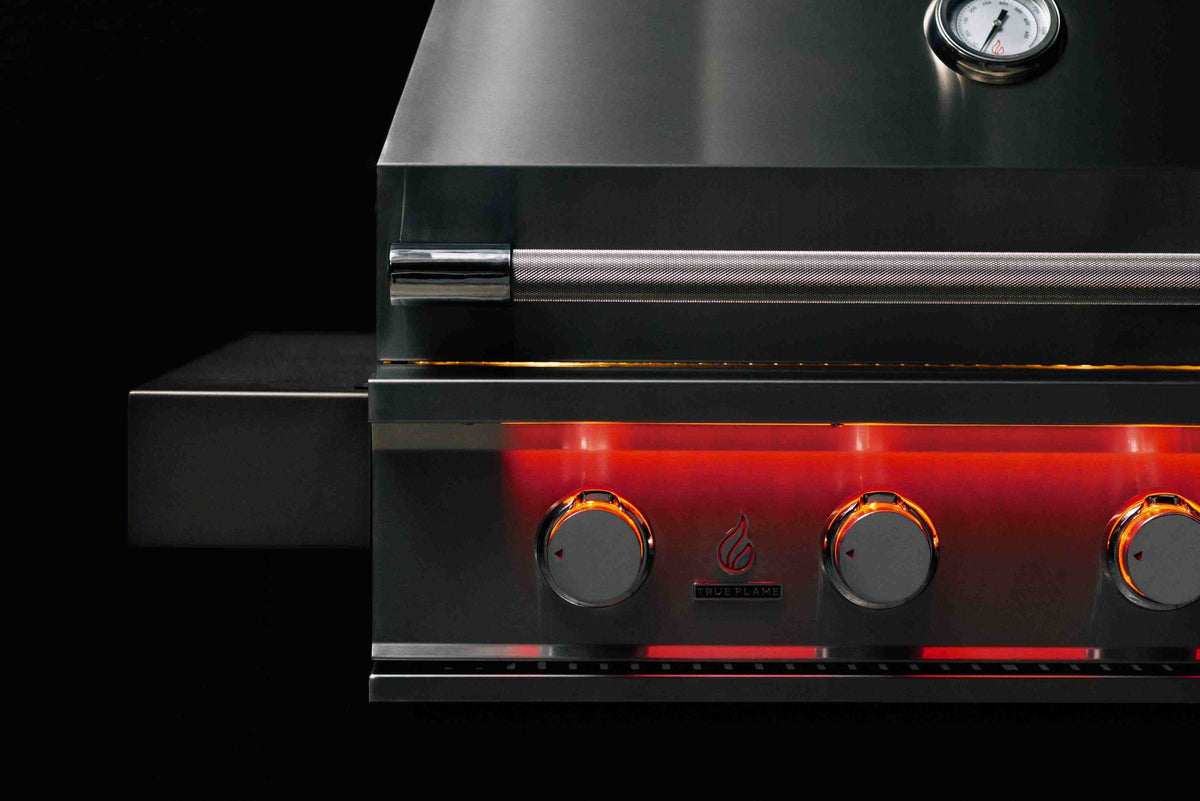 Stainless built-in propane gas grill control panel with four burner knobs and red glow
