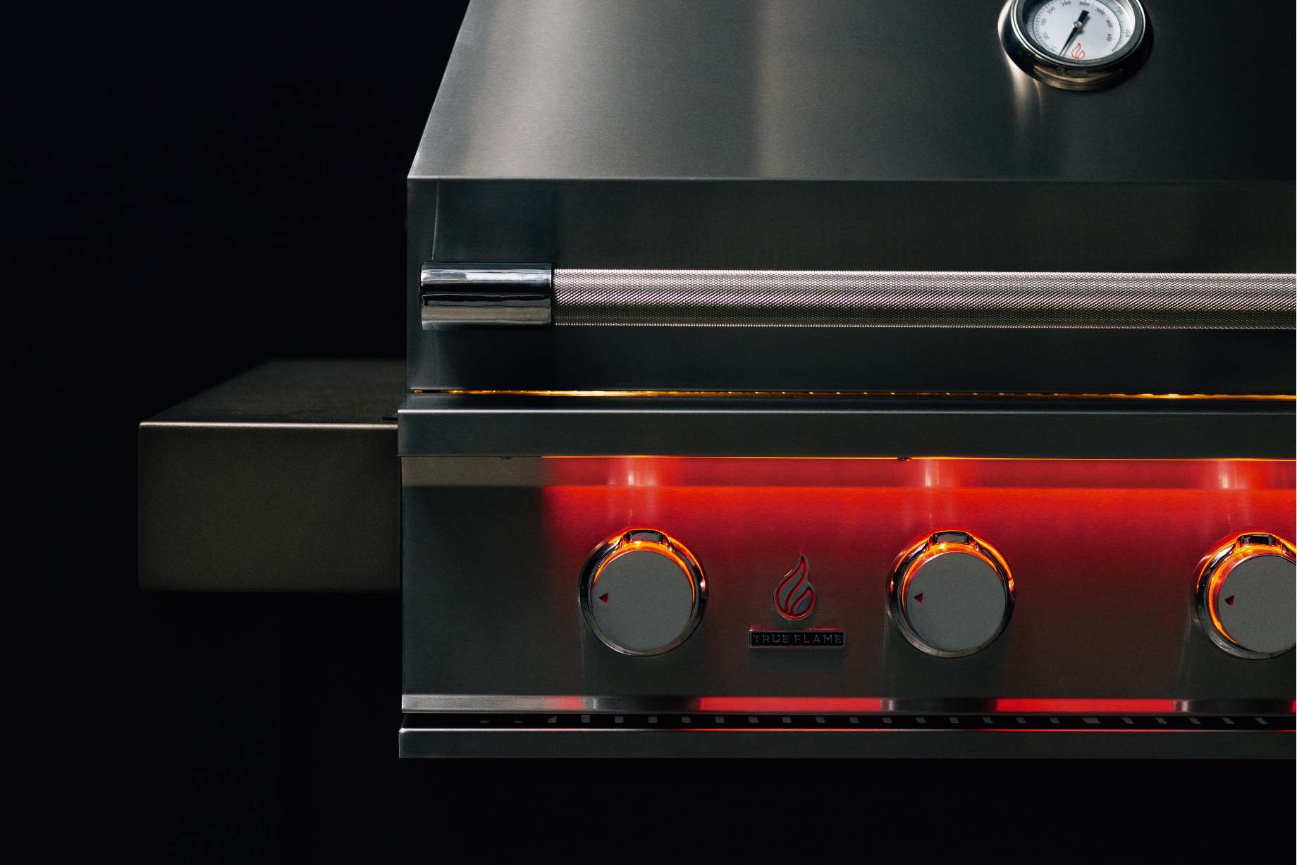 Close-up of front control knobs with red glow and thermometer on stainless grill lid