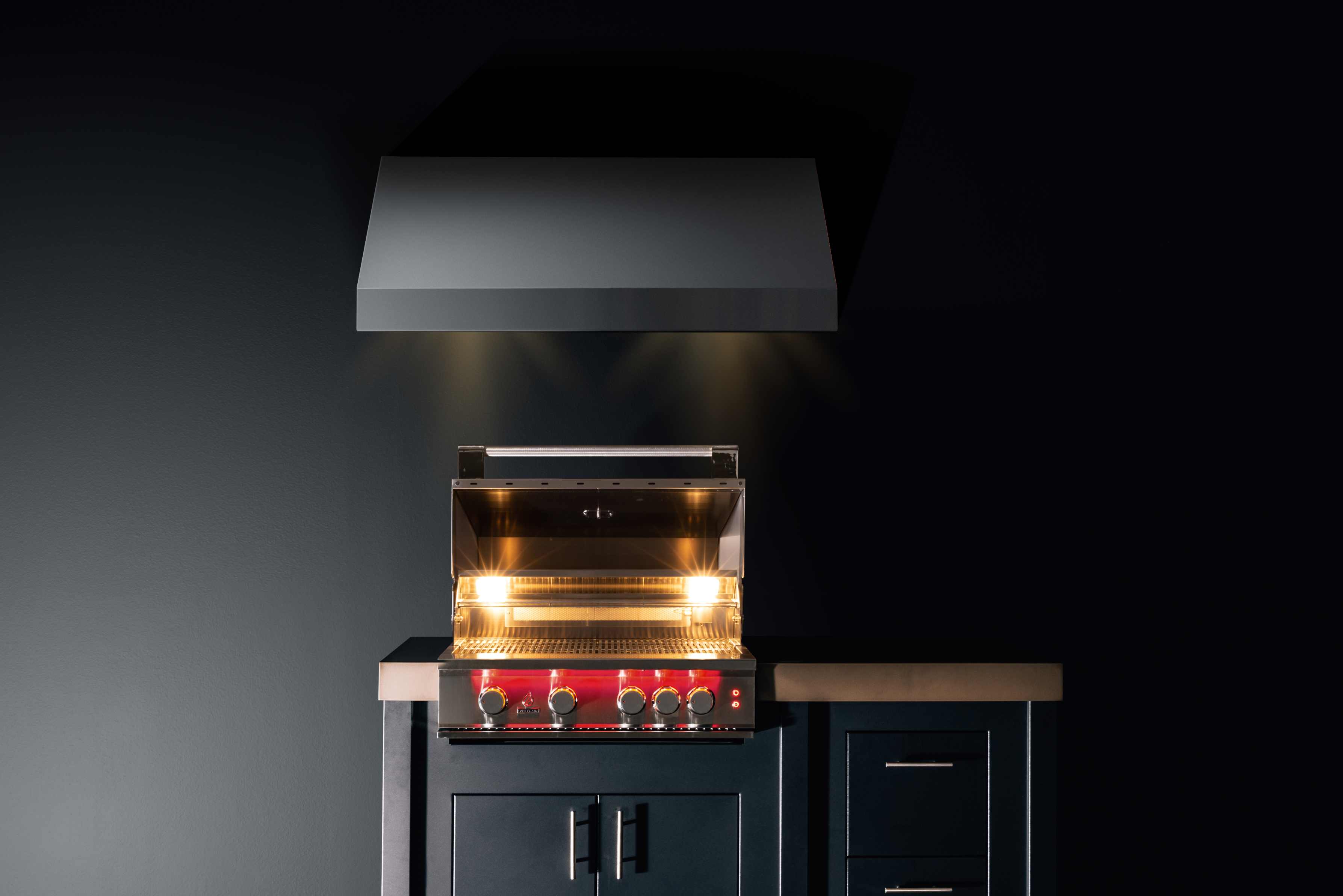 Built-in stainless gas grill with hood open, glowing burner bars and control knobs
