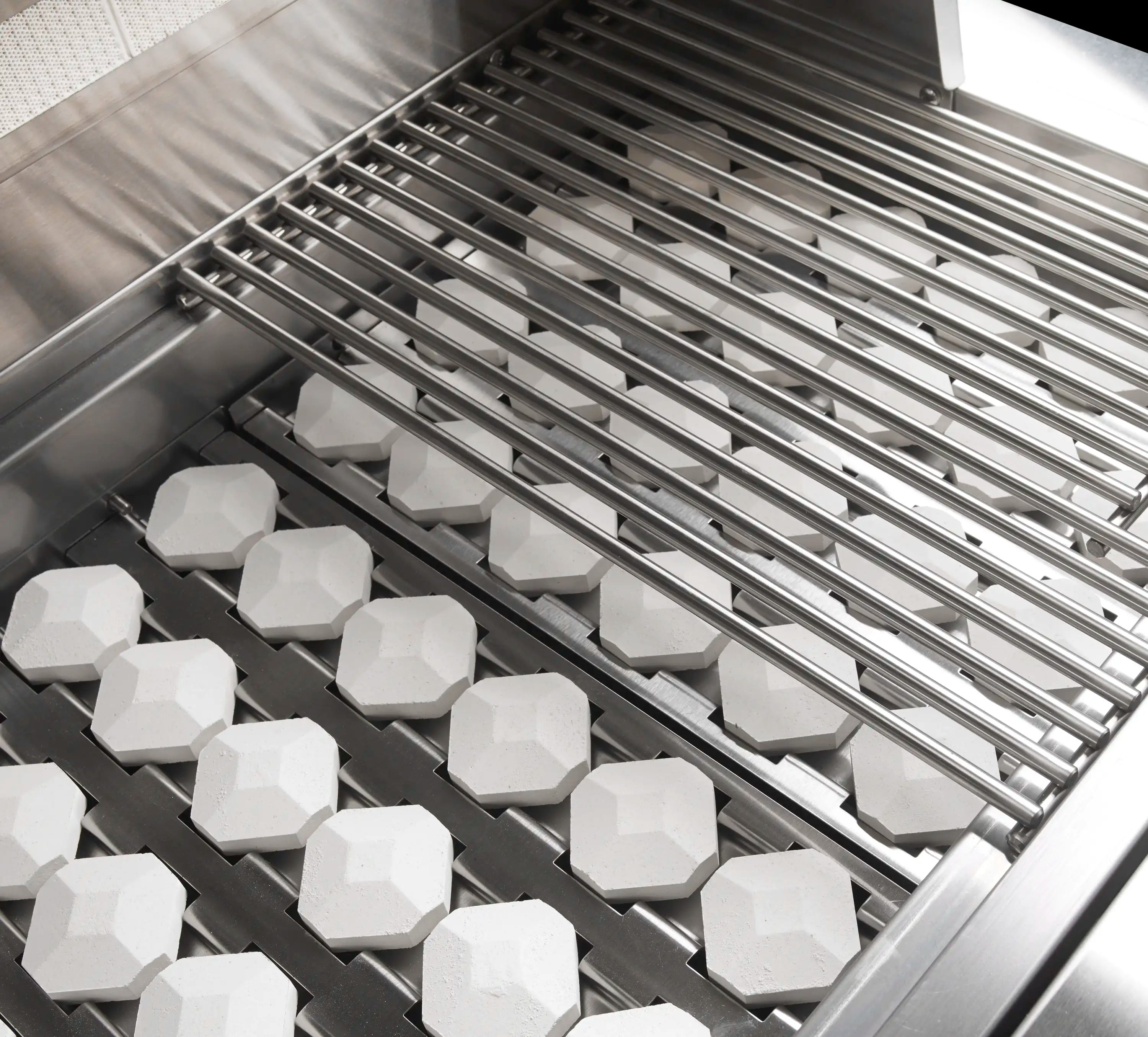 Stainless steel grill with cooking grates over hexagonal white briquettes