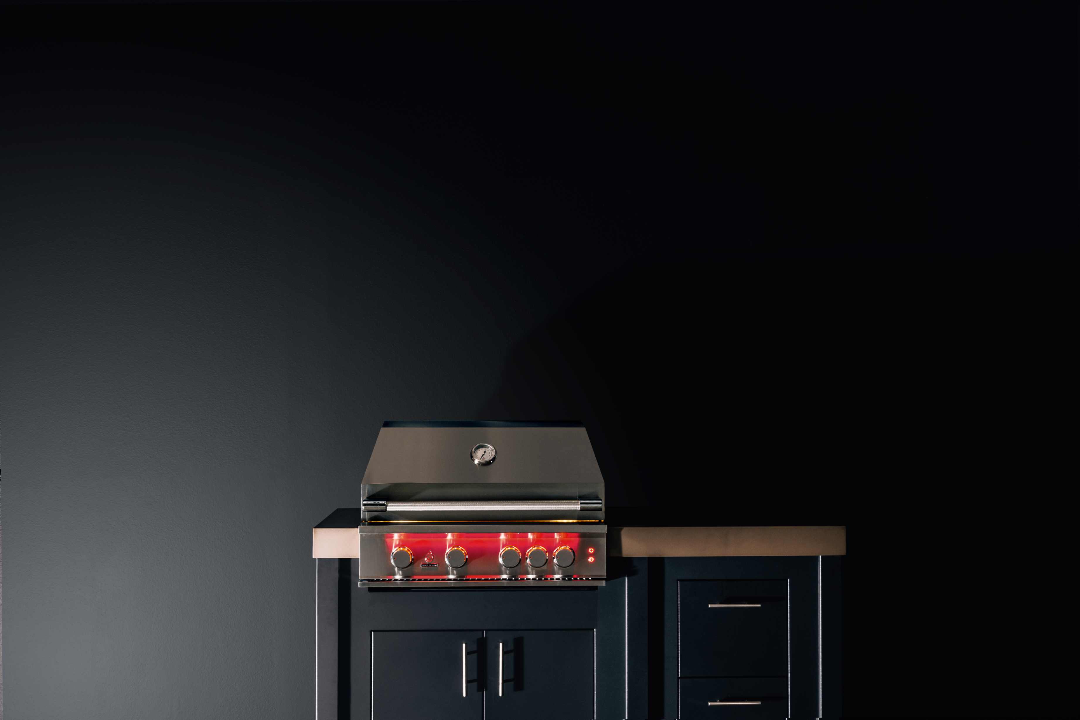 Stainless gas grill with hood, red-lit controls, and built-in cabinet