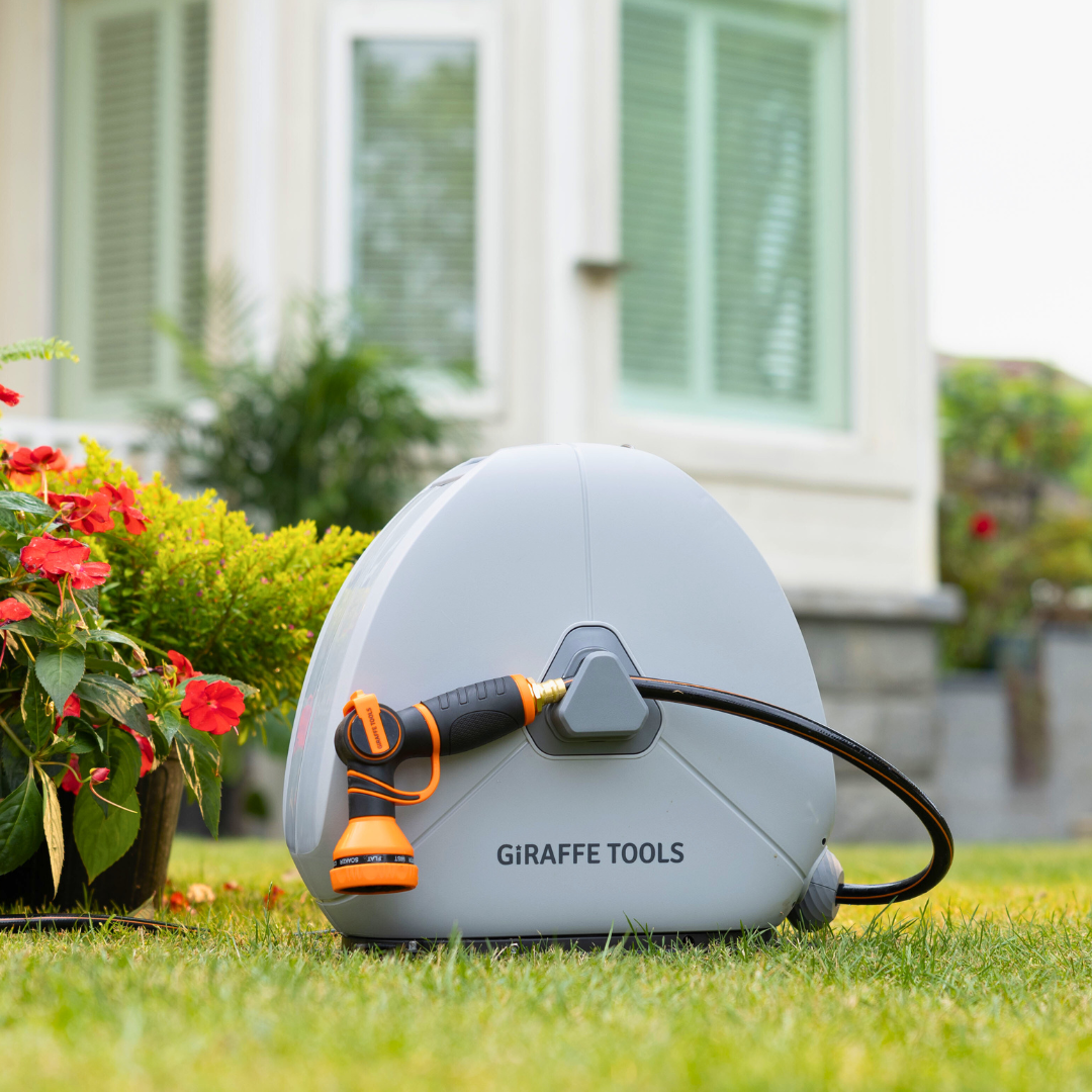 Ground-mounted retractable hose reel with white housing, black base, and orange nozzle on grass