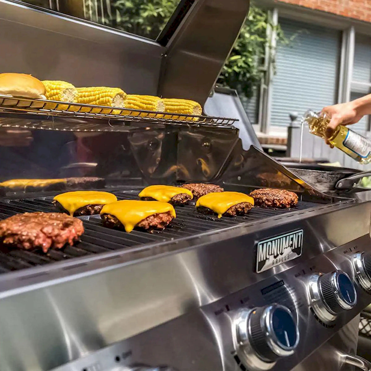 Burgers on grill grates with lid open above stainless steel hood