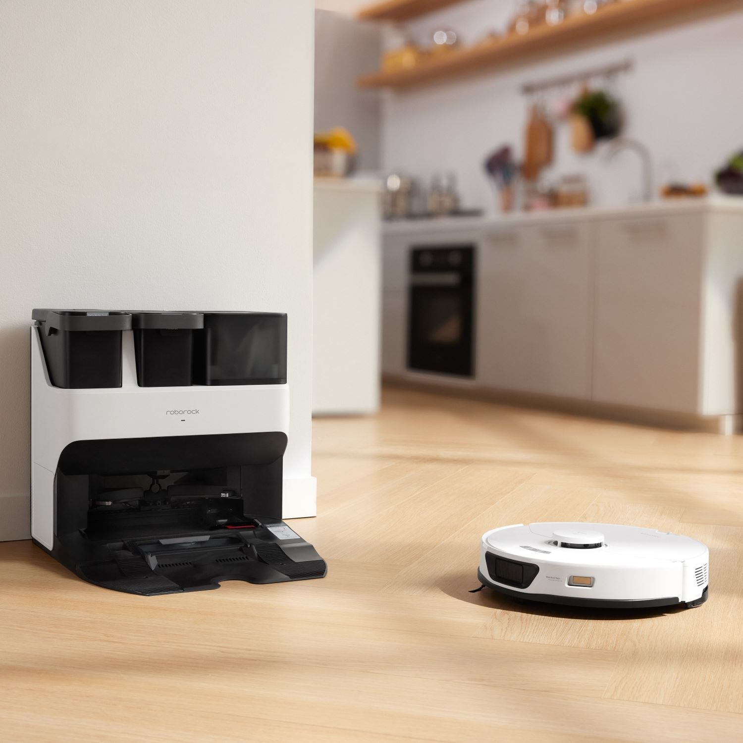 White robot vacuum near charging dock on hardwood in a bright kitchen