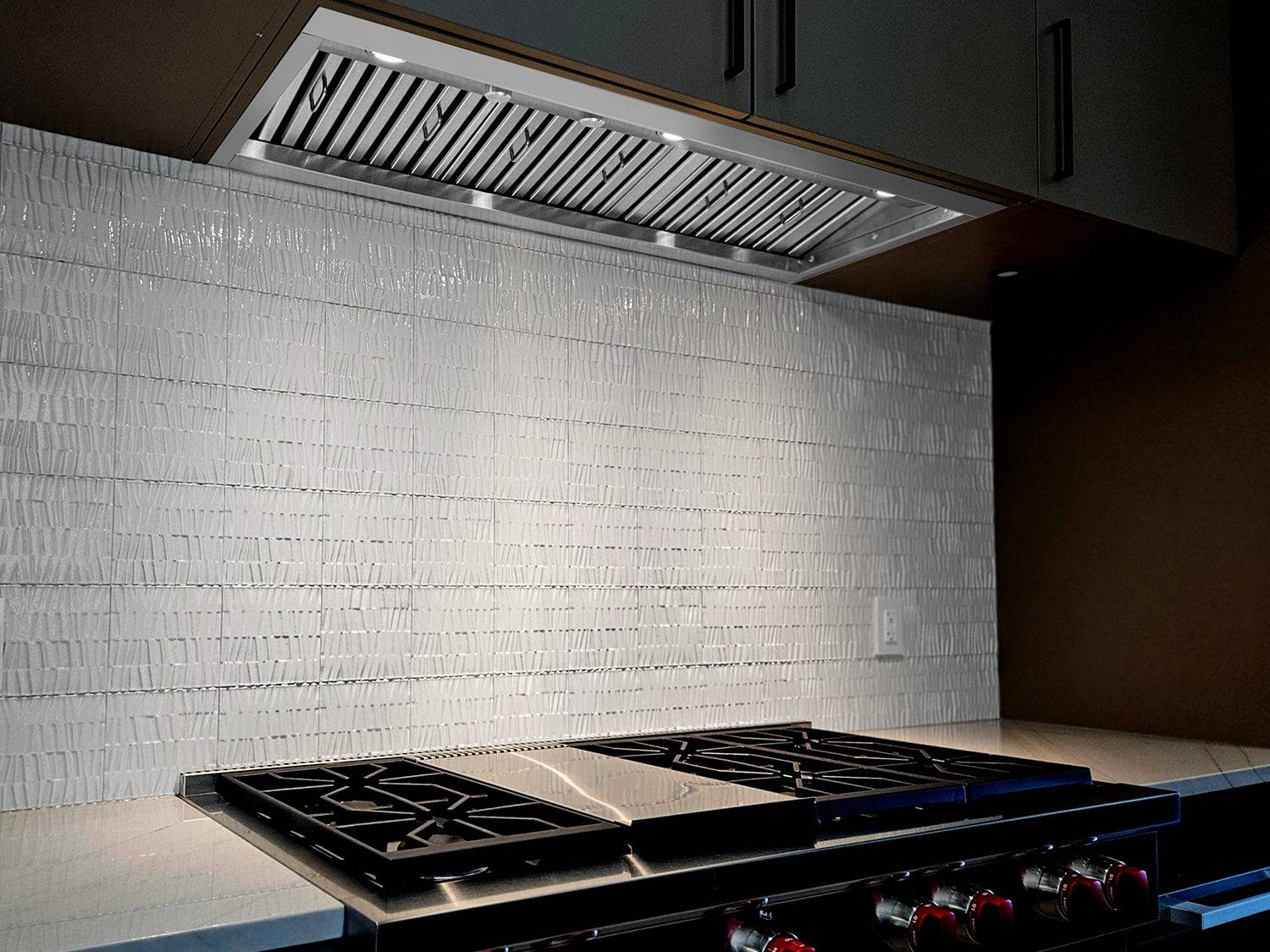 Stainless steel insert range hood above cooktop with vent grille and control knobs