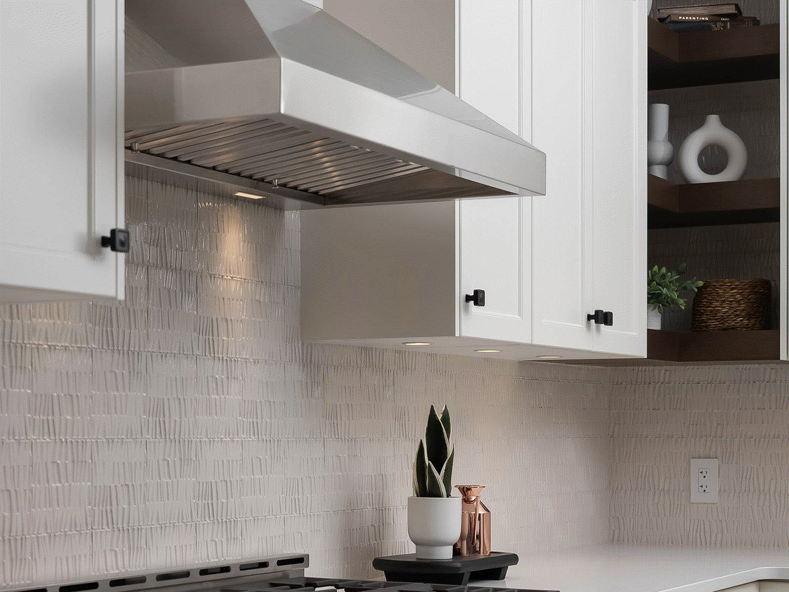 Stainless steel wall range hood mounted under kitchen cabinet with vented underside