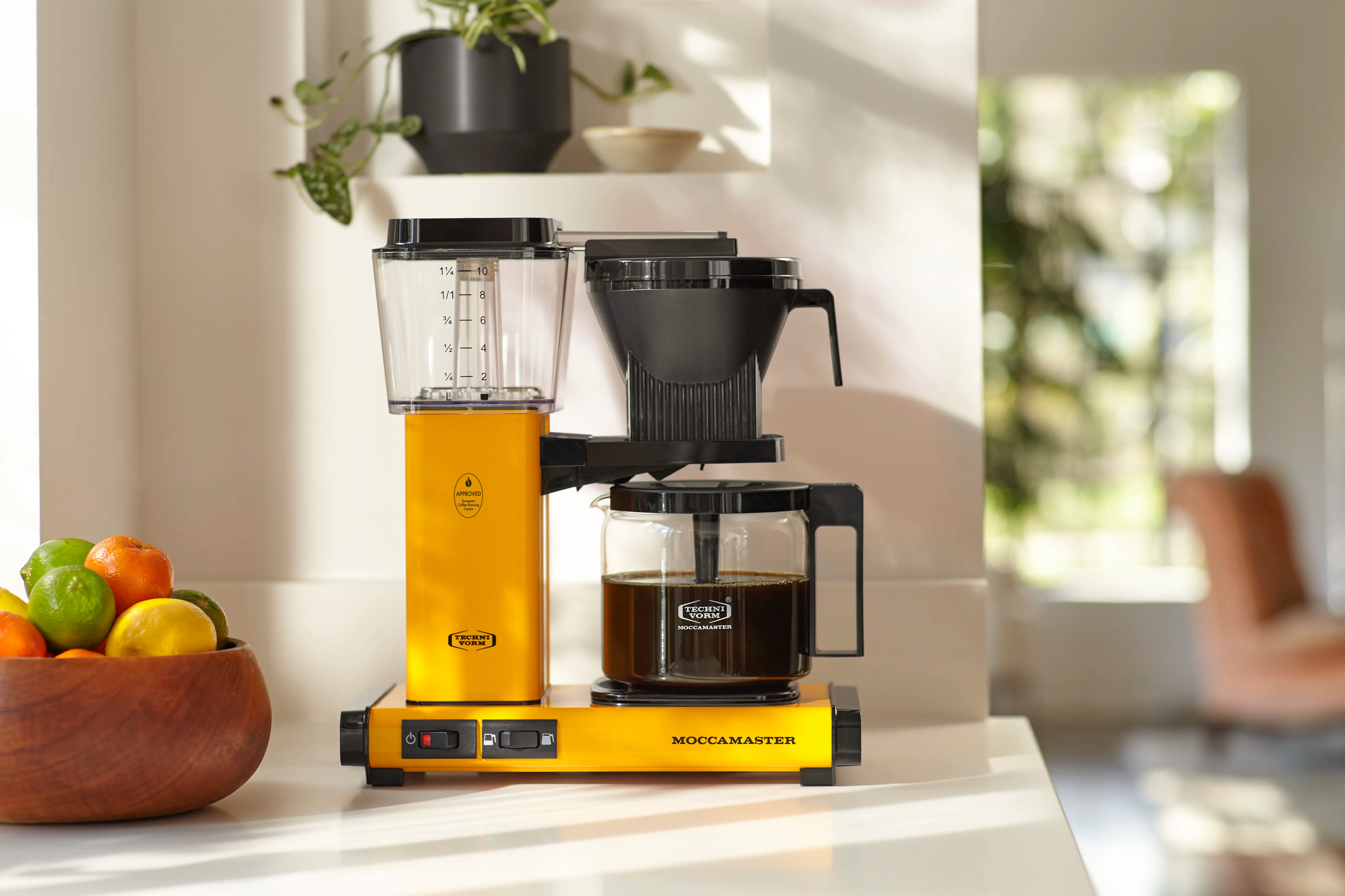 Yellow drip coffee maker with glass carafe, black brew basket, and control panel