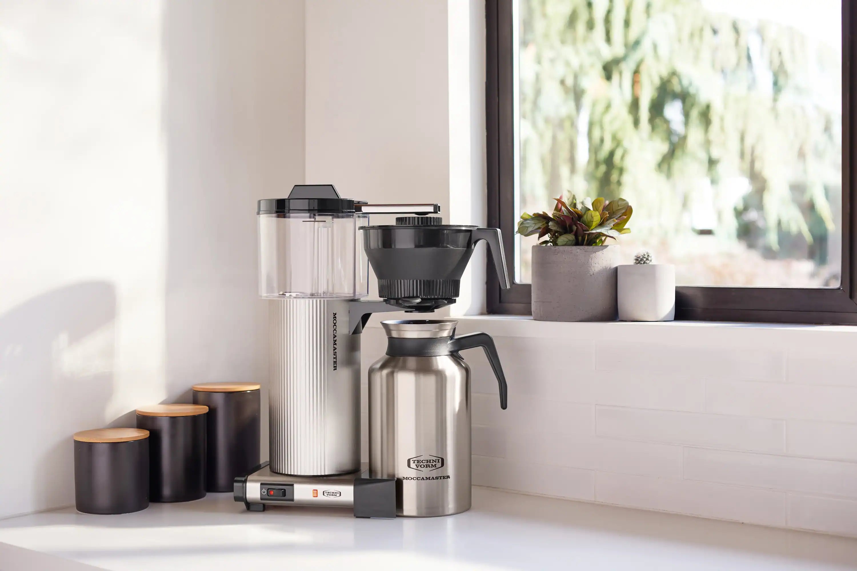 Brushed silver coffee maker with drip-stop handle, black funnel, and metal carafe
